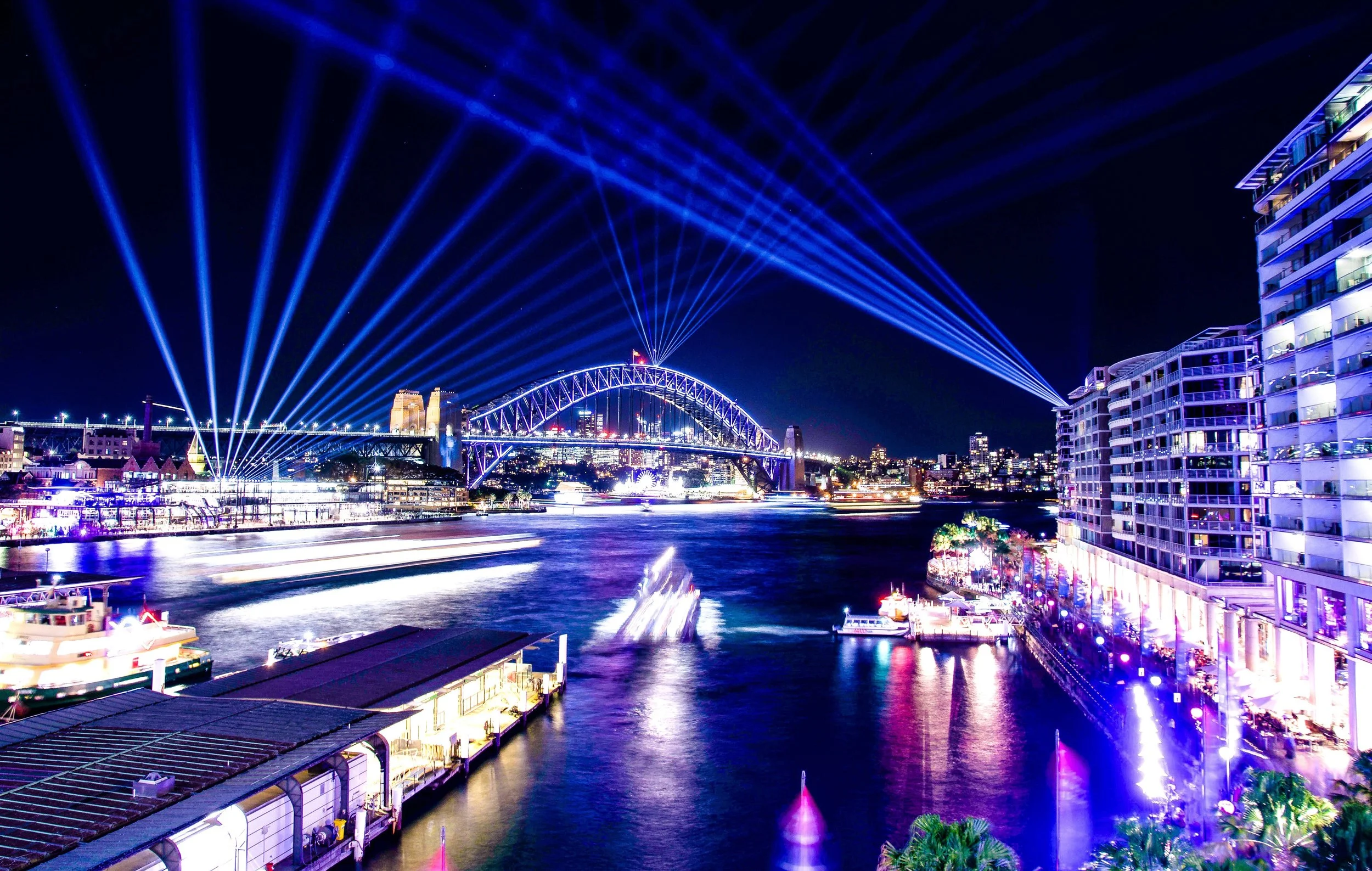 Sydney Harbour at night glows with light projections across the Harbour Bridge and waterfront, capturing the vibrancy of events, tourism and city life.
