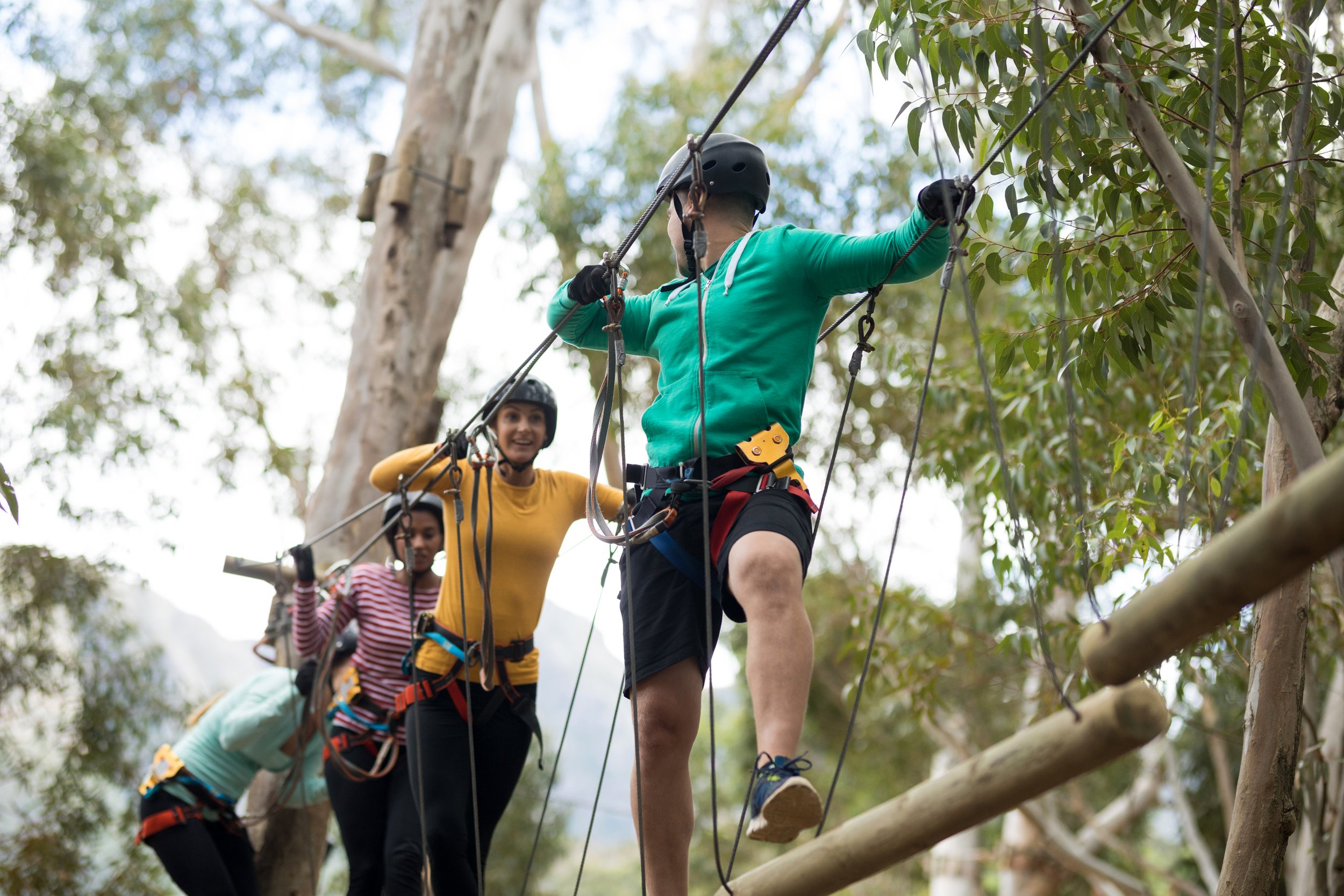 A participant navigates a high ropes course with safety harness and helmet, supported by an instructor, illustrating adventure product and experience development.