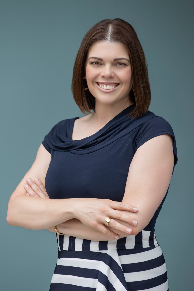 Portrait of Giovanna Lever smiling confidently with arms crossed, wearing a navy top against a soft blue background.