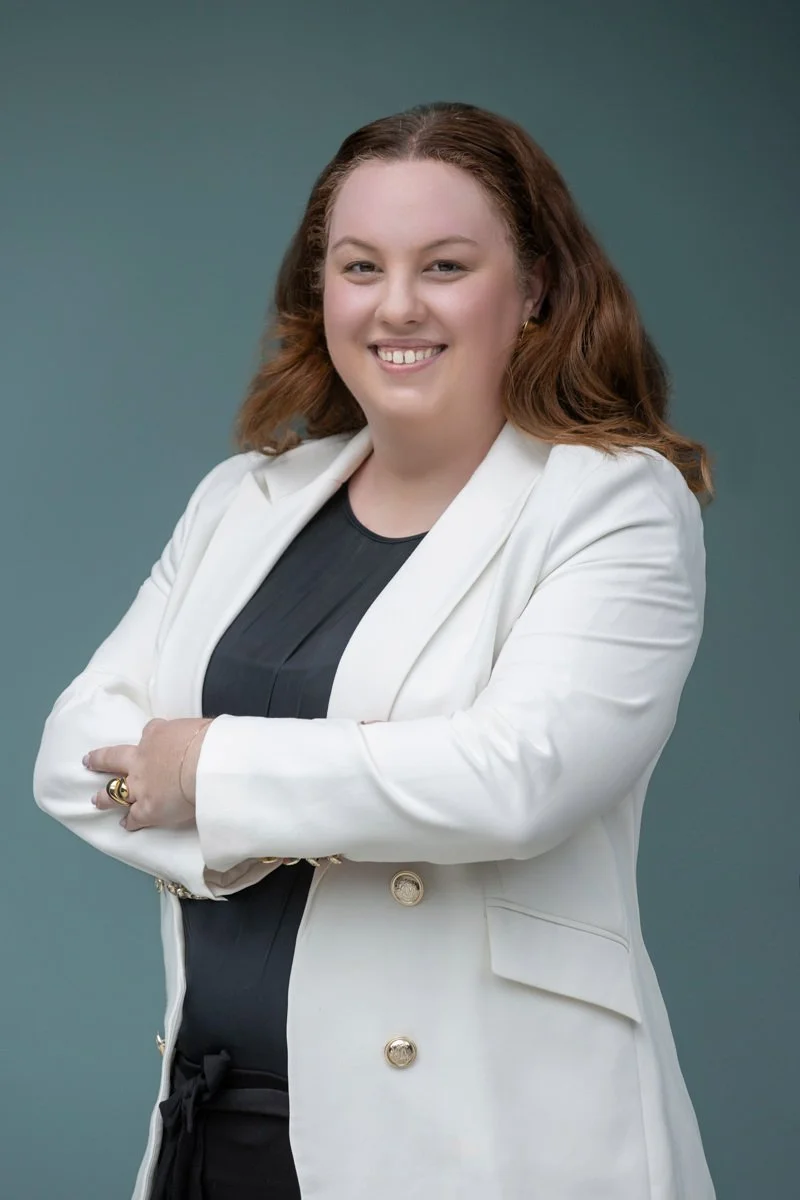 Portrait of Jackie Hicks smiling with arms crossed, wearing a light blazer against a soft blue background.