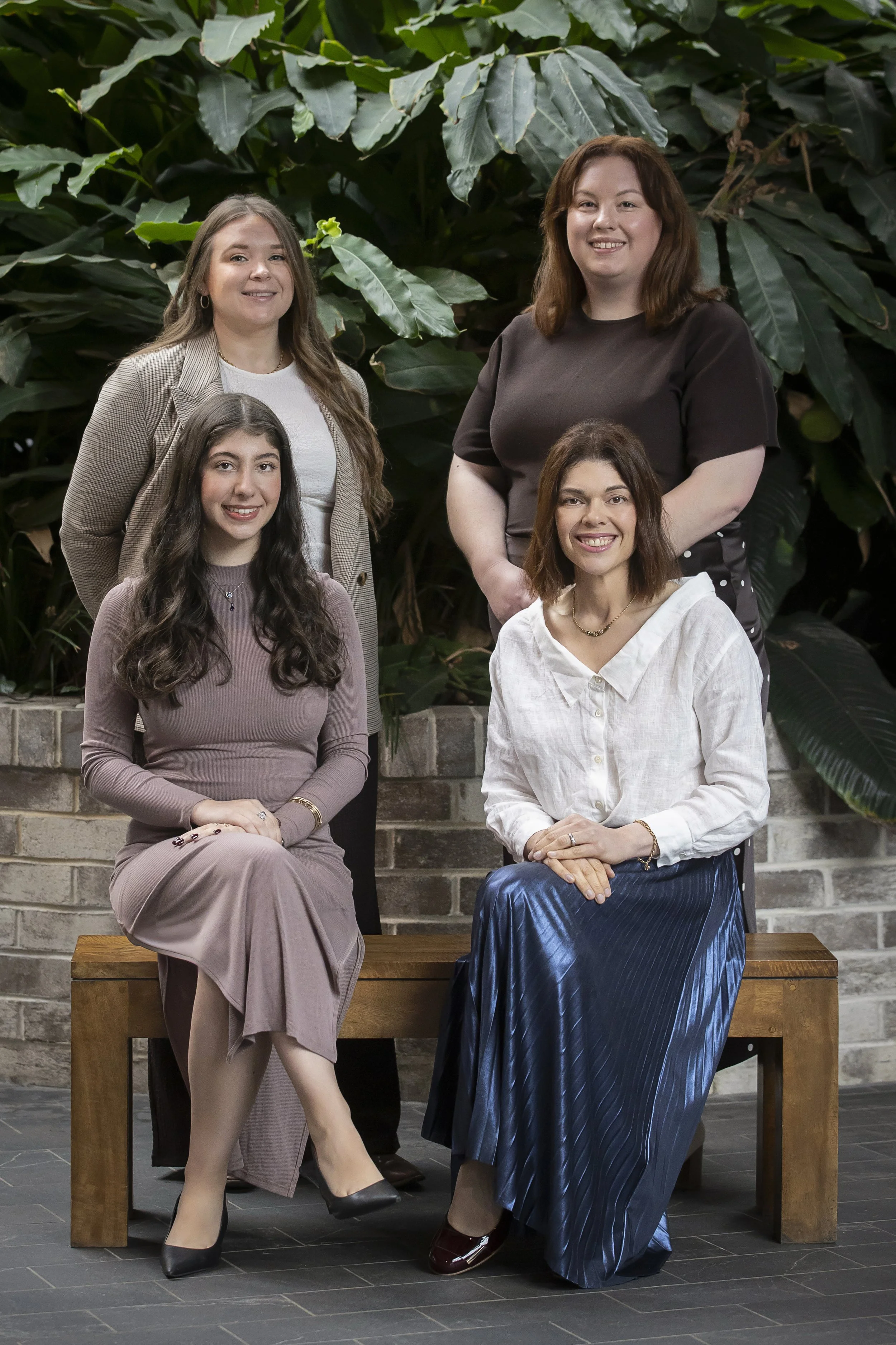 Four Sparrowly Group team members smiling together in front of lush green foliage.