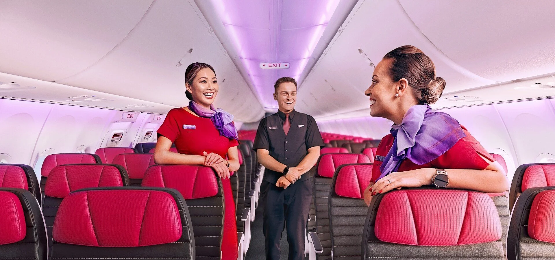 Three Virgin Australia Flight Attentants  standing in the seating area of a plane.