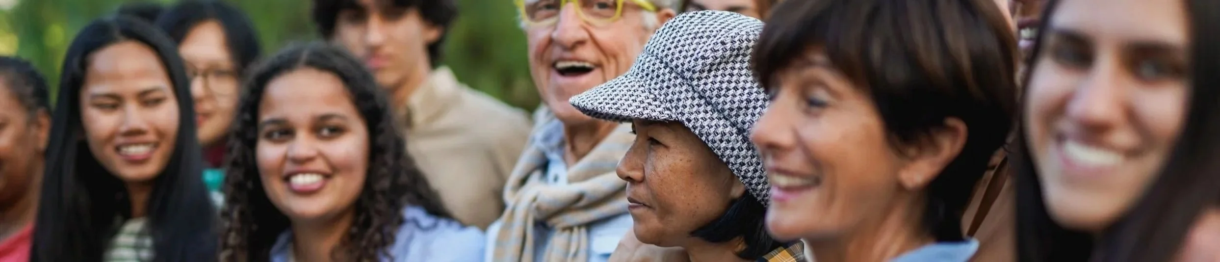 A diverse group of people smile and engage in conversation, representing community connection, inclusion and shared experience.