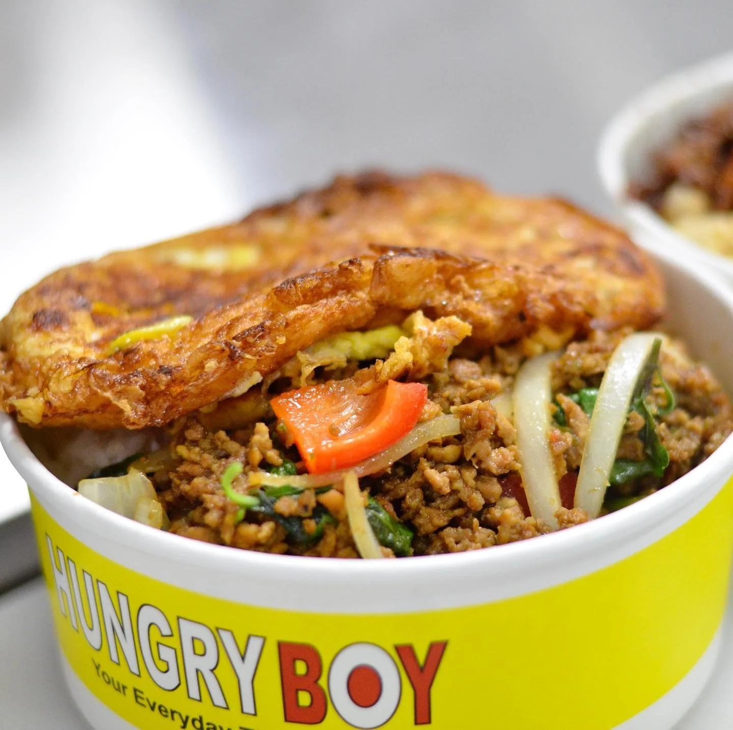 Close-up of a bowl of ground beef with vegetables, topped with a fried egg, and a yellow label that says "HUNGRY BOY".