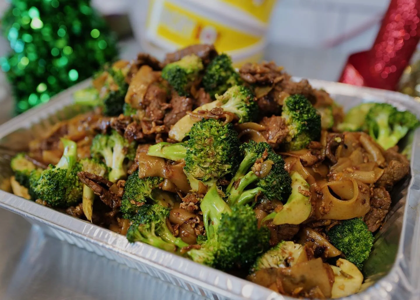 Stir-fried beef with broccoli and flat rice noodles in a foil container.