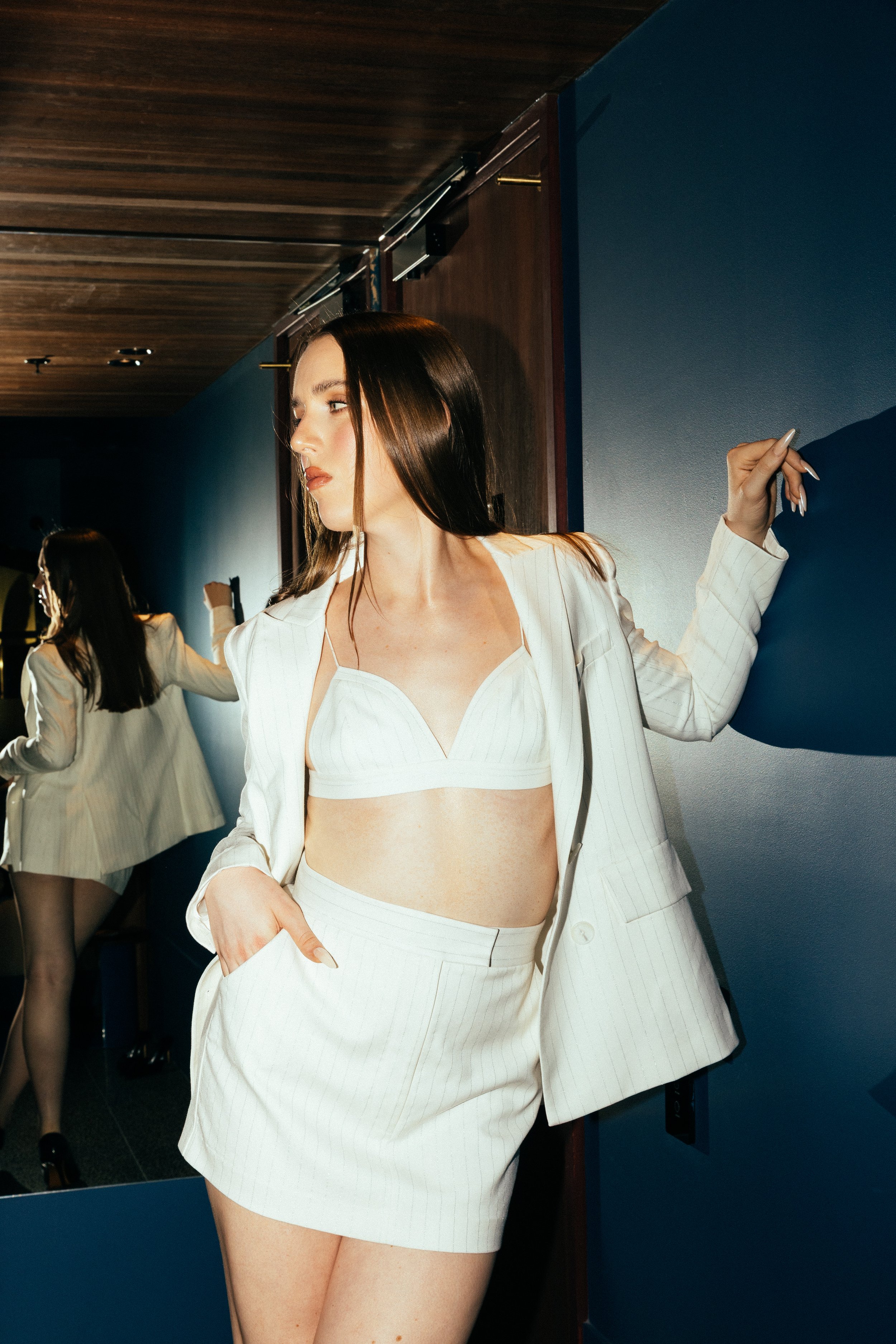 Riley Rose, a high-end transgender companion, wearing a white blazer and skirt in a composed indoor setting.