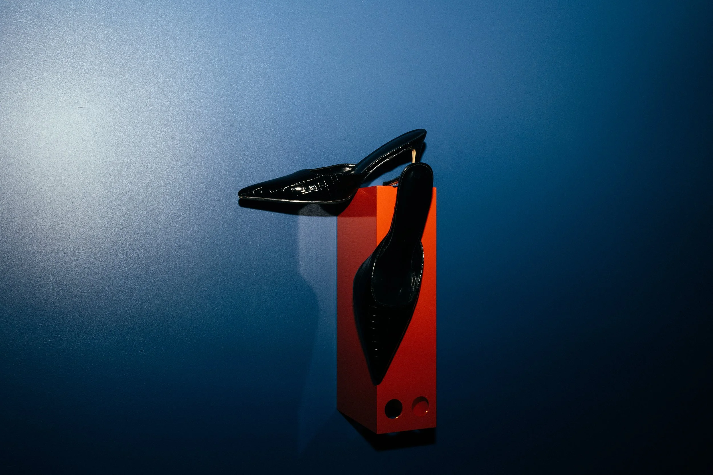 Black high-heeled shoes displayed on a pedestal against a blue backdrop.