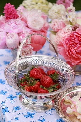 An elegant reticulated silver basket filled with strawberries on a d porthault tablecloth and pink peonies around.