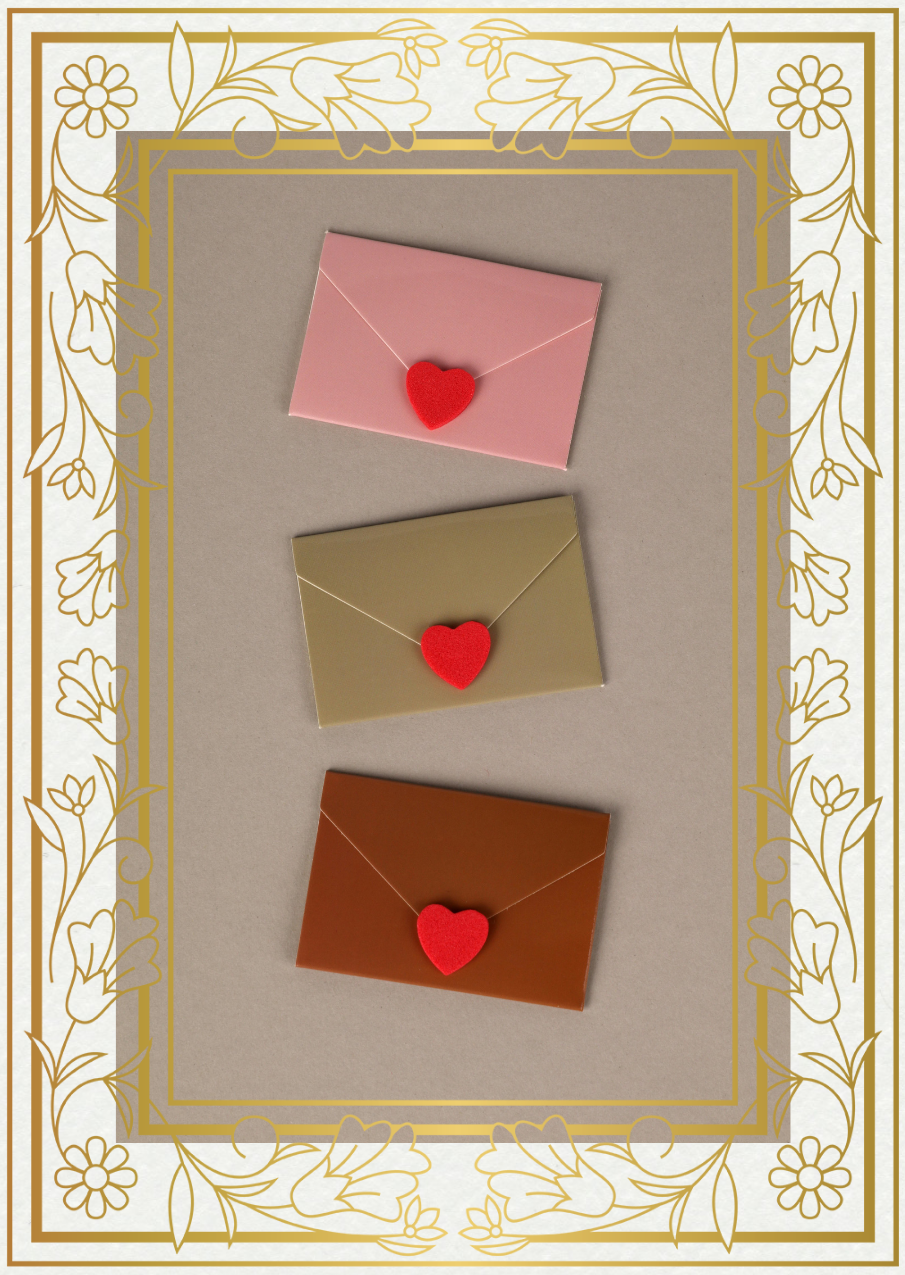 Three colored envelopes (pink, gold, copper) each sealed with a red heart sticker, arranged vertically on a gray surface with a decorative floral gold border.