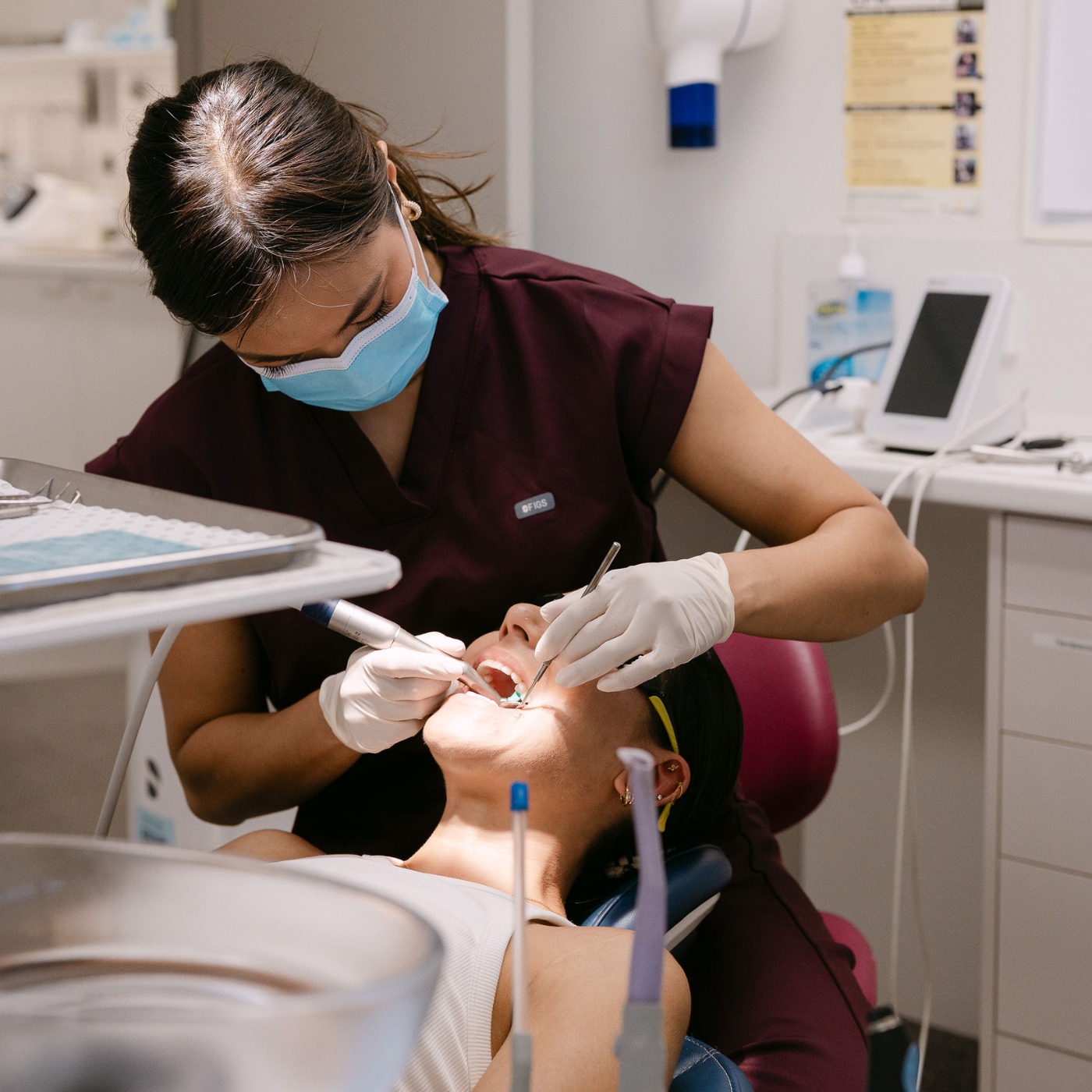 Dental professional wearing a face mask and gloves performing a dental procedure on a patient lying in a dental chair.