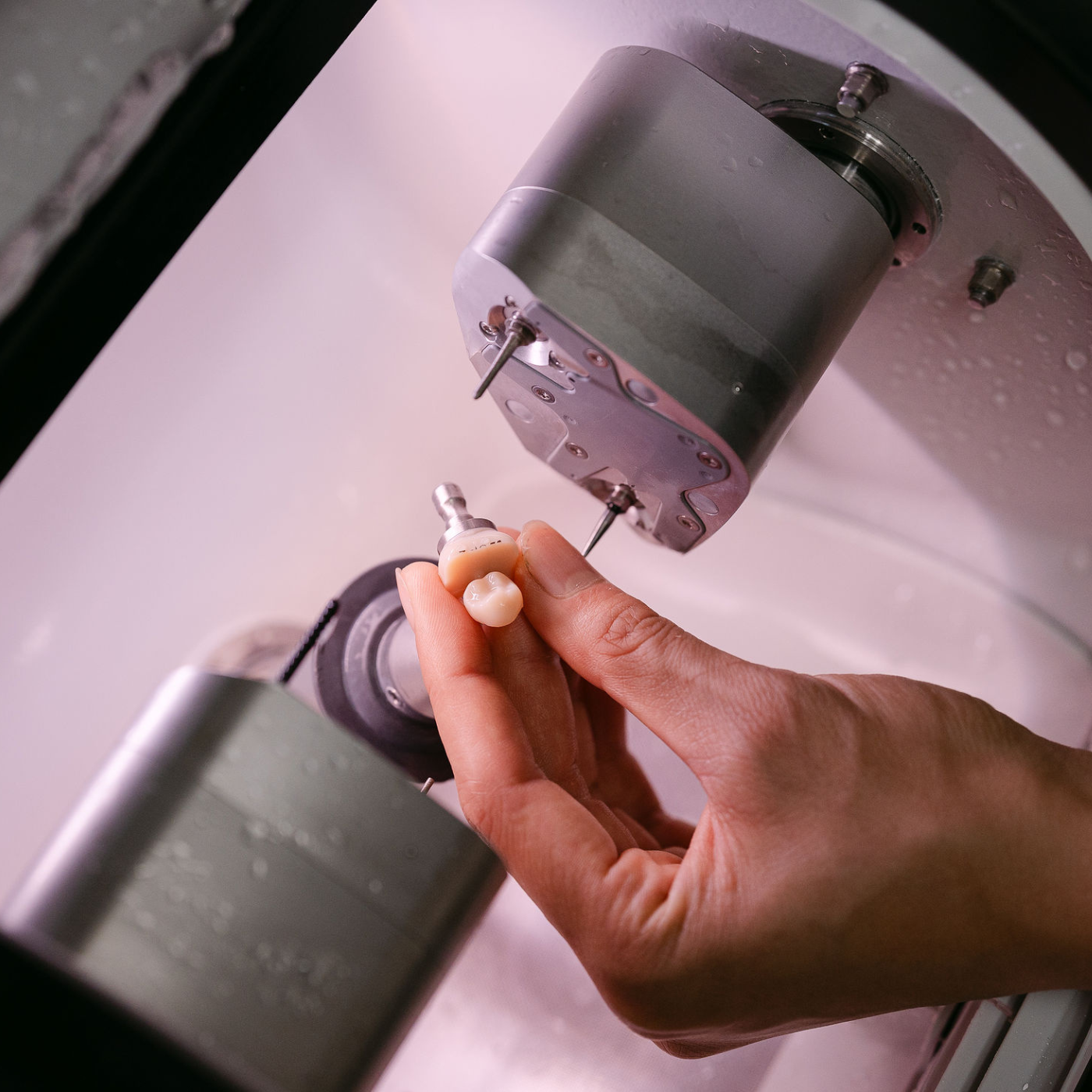 Dentist holding a dental implant or prosthetic inside a milling machine.
