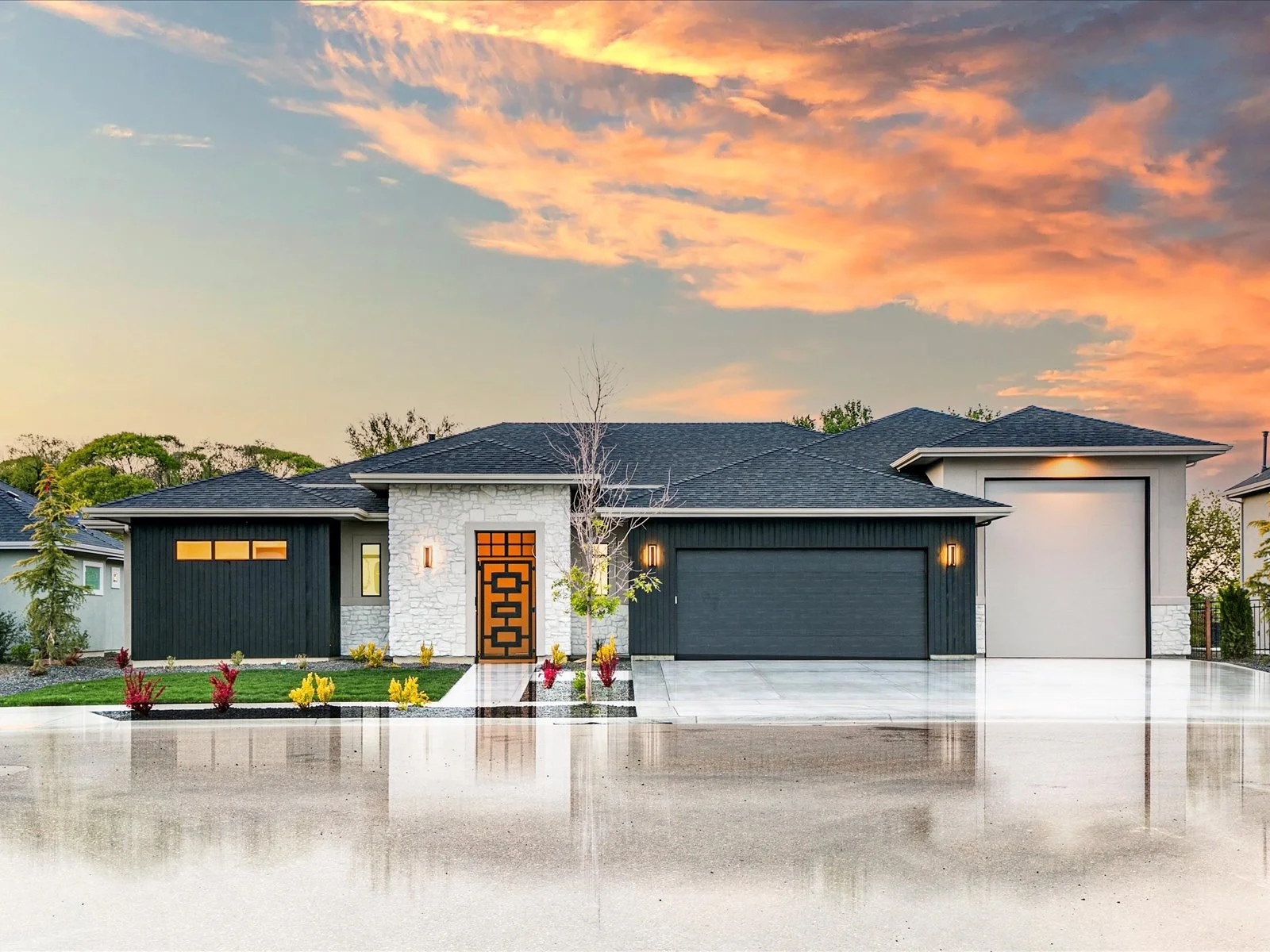 Modern house with black and white exterior, landscaped front yard, and sunset sky in the background.