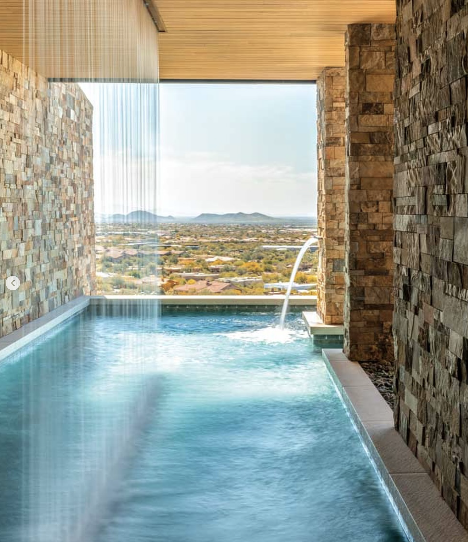swimming pool with water wall waterfall looking out onto a cityscape and mountains in the distance, stone and wood interior design.