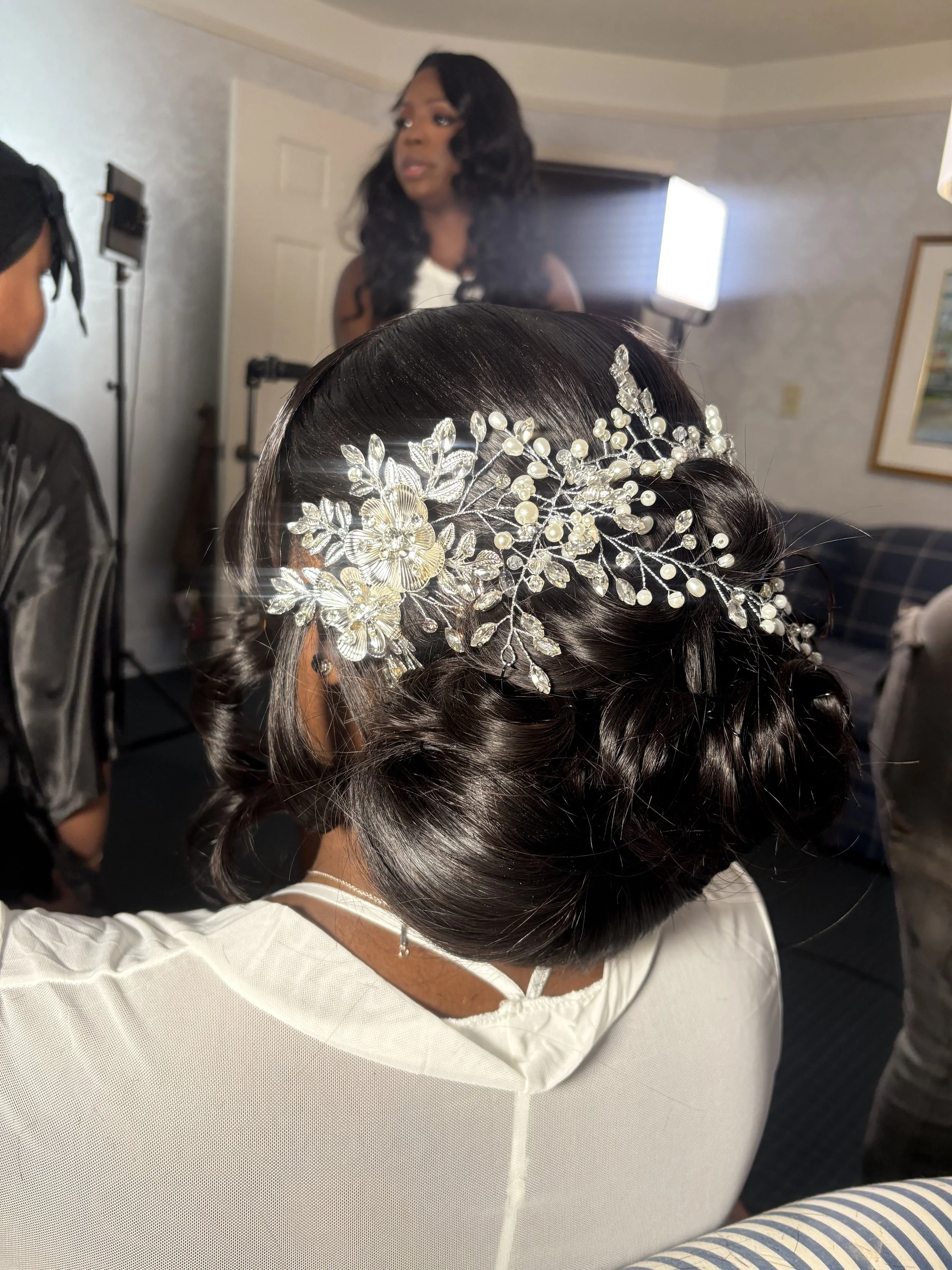 Close-up of a woman with dark, styled hair wearing an ornate silver and pearl headpiece, with a bridal or formal gown.