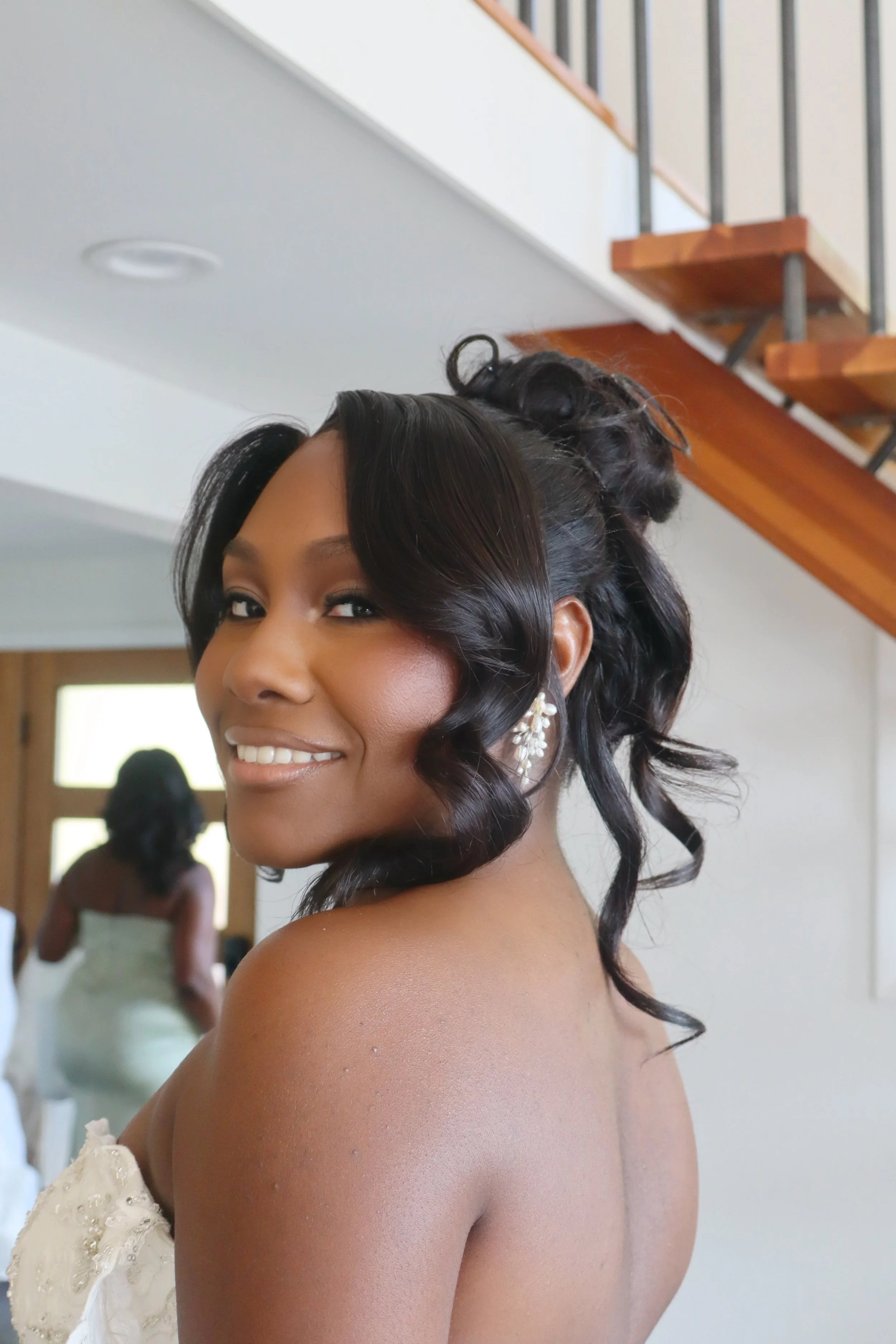 A woman with styled black hair and jewelry smiling at the camera indoors.