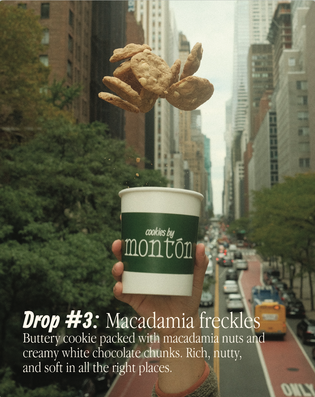 Hand holding a coffee cup with the words "cookies by monton" printed on it, with a handful of macadamia cookies being dropped into the cup against an urban city street background.
