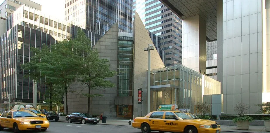 City street scene with yellow taxis, modern office buildings, and a tree in front.