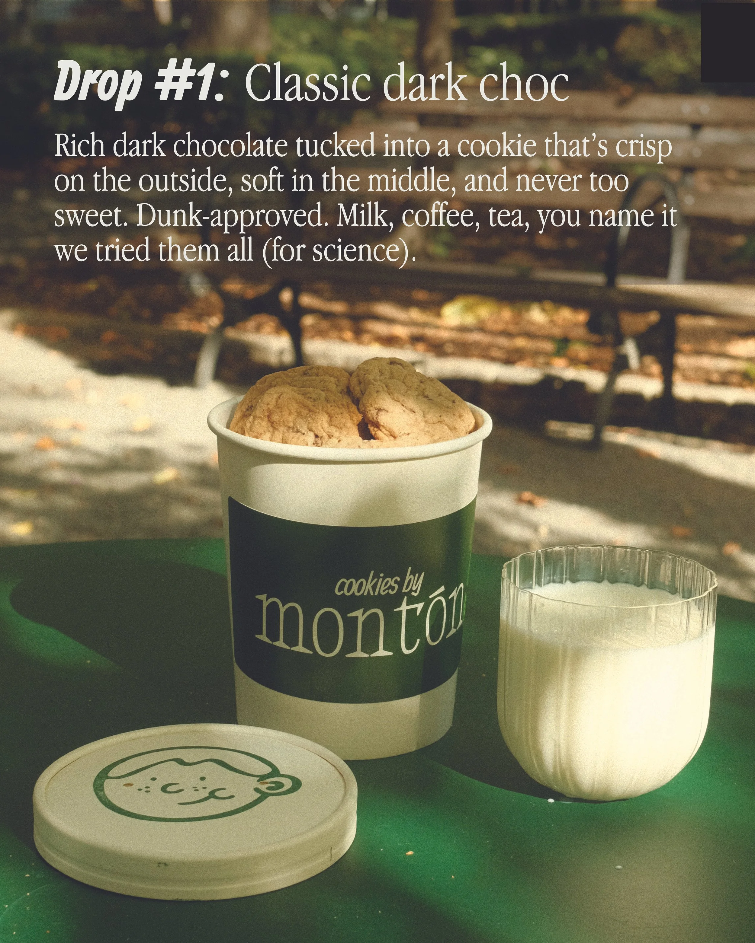 A cup of cookies by montón with three cookies on top, a glass of milk, and a sealed container with a face on it, sitting on a green surface outdoors with a park bench and trees in the background.