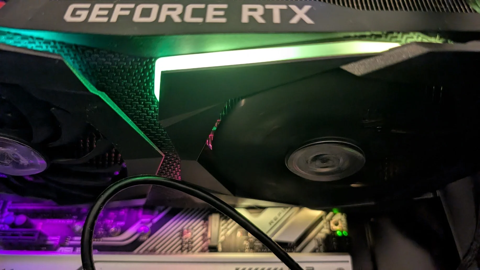 Close-up of a computer's graphics card inside a PC case, illuminated with multicolored RGB lighting, with visible NVIDIA GeForce RTX branding on top.