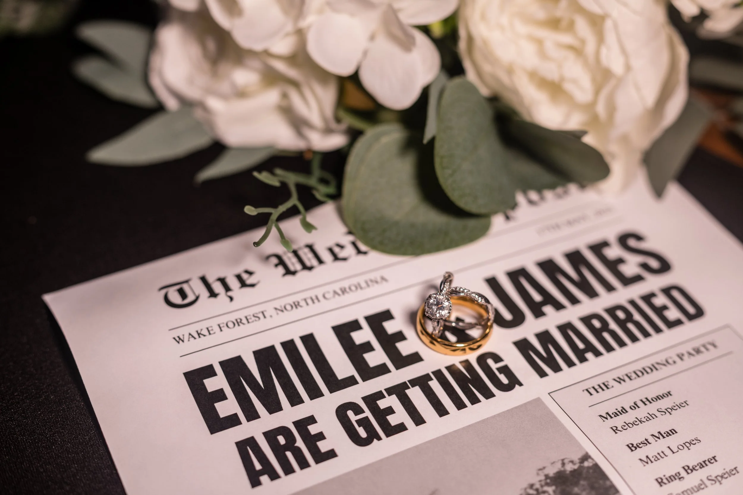 Wedding announcement with a bouquet of white flowers and greenery, a diamond engagement ring and a wedding band on top of the newspaper.