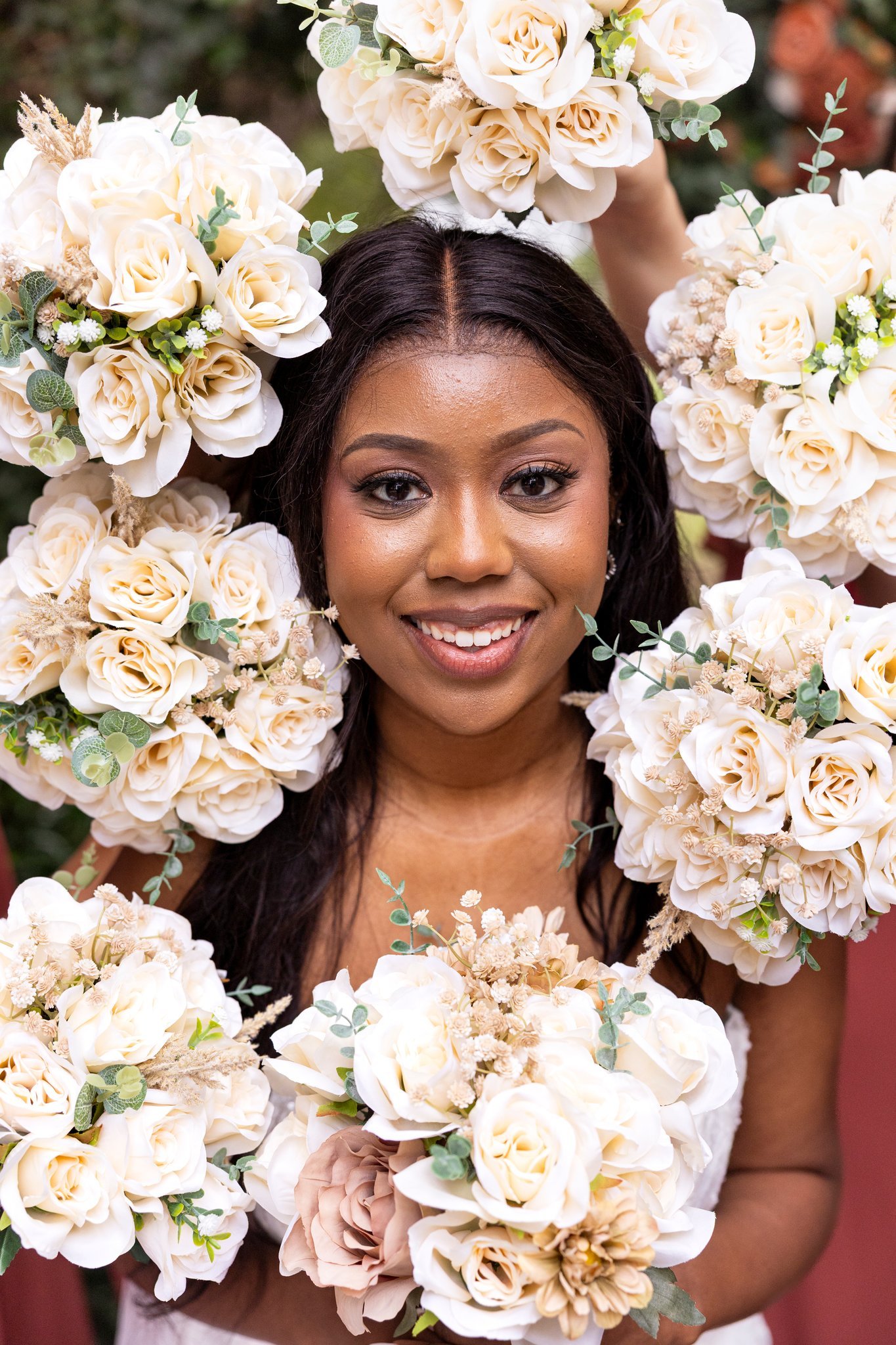 A woman with long dark hair and a smile holding or surrounded by white and beige flower bouquets, including roses and greenery.