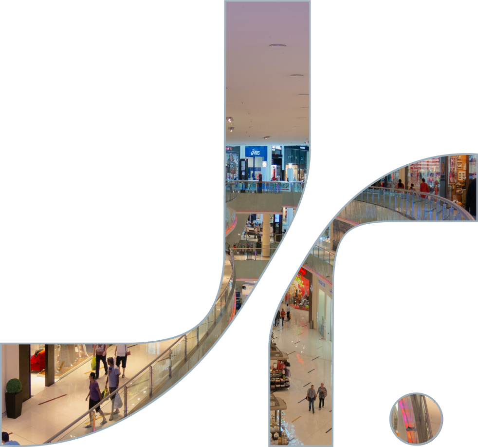 Interior of a shopping mall with multiple levels, storefronts, shoppers walking, and store signage.