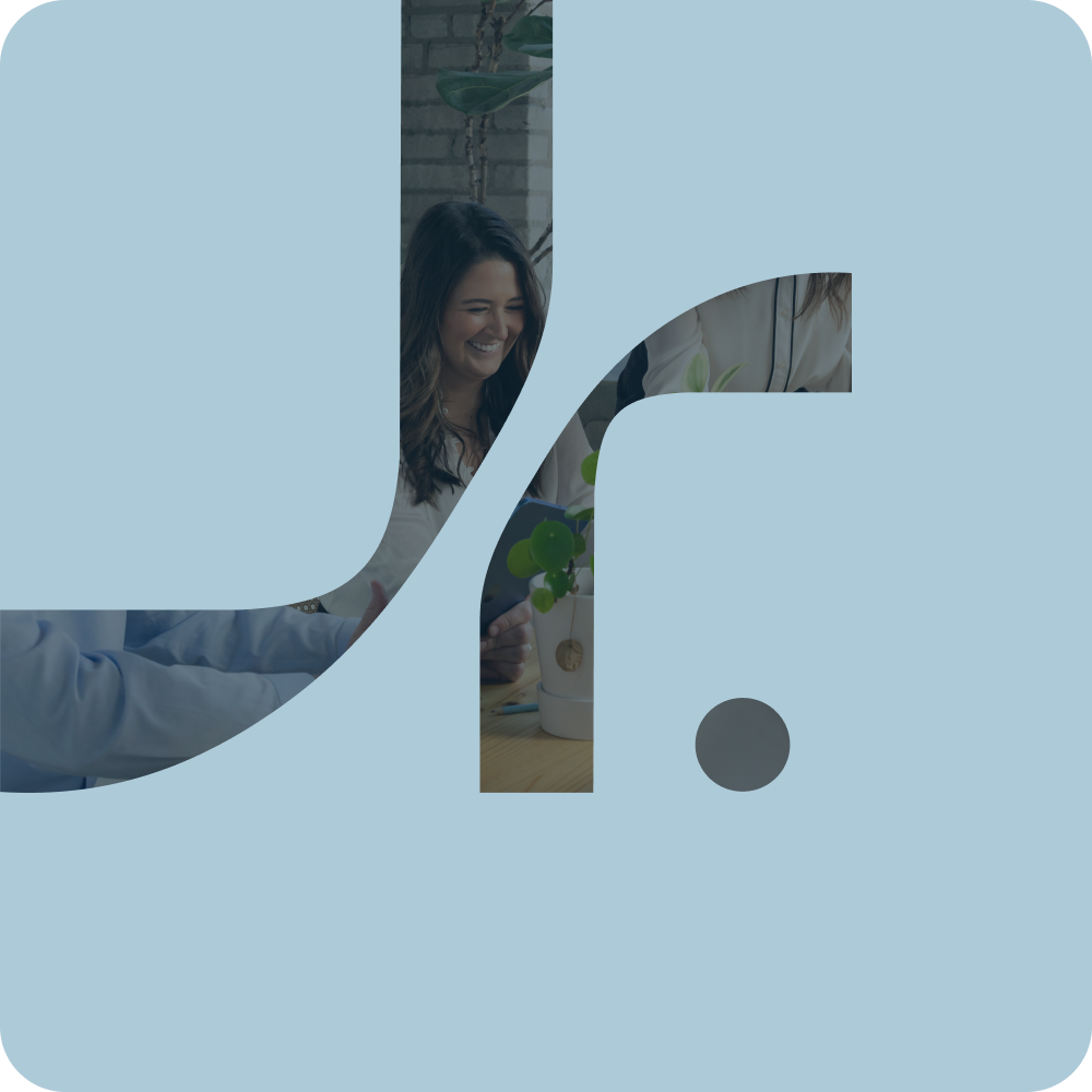 A woman smiling and talking to another person in an indoor setting, with a potted plant and a brick wall in the background.