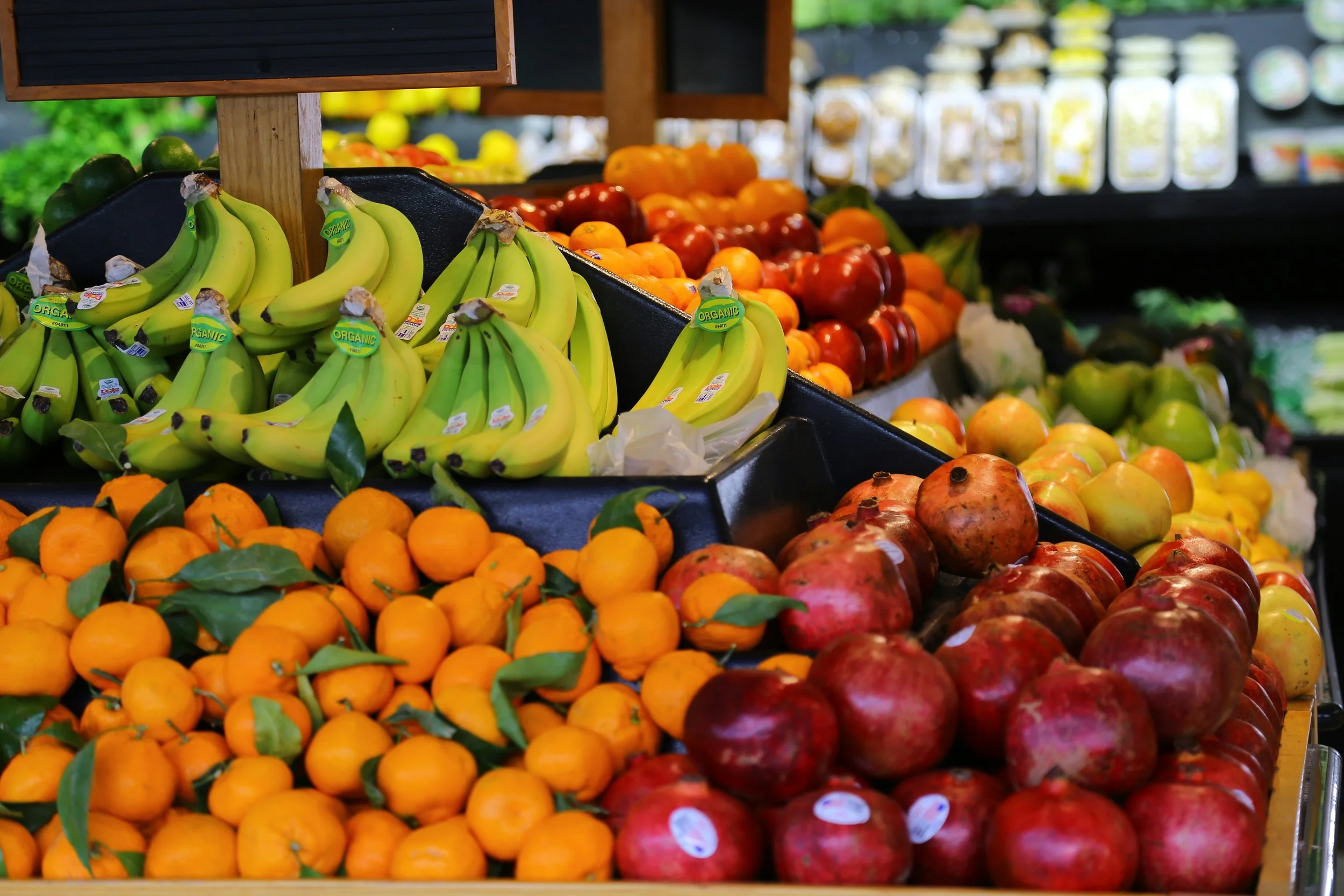 Fresh bananas, oranges, pomegranates, and other fruits displayed at a grocery store produce section.