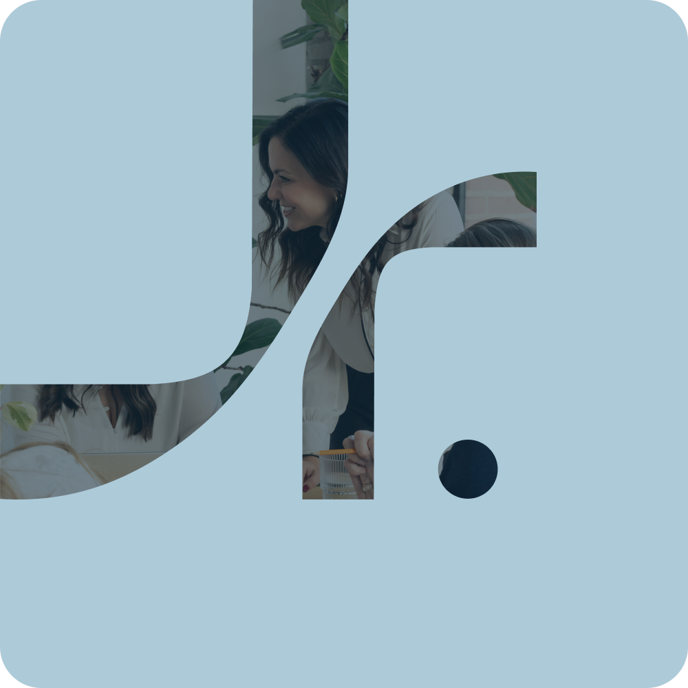 A woman with dark brown hair smiling and talking to a person with brown hair at a table, with large green plants in the background, seen through a cut-out of a stylized lowercase 'f' on a light blue background.