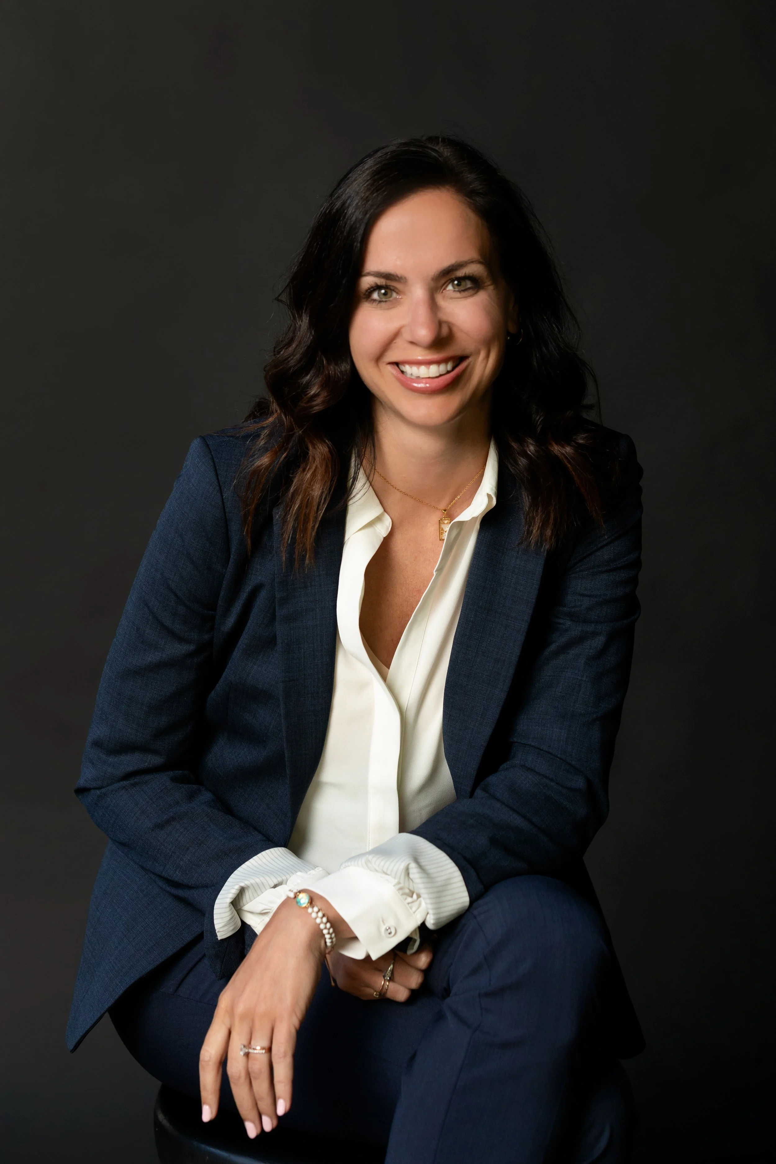 Jenn Hahn, founder of J Recruiting dressed in a navy blazer and white blouse, seated against a dark background. Available for press and speaking engagements.
