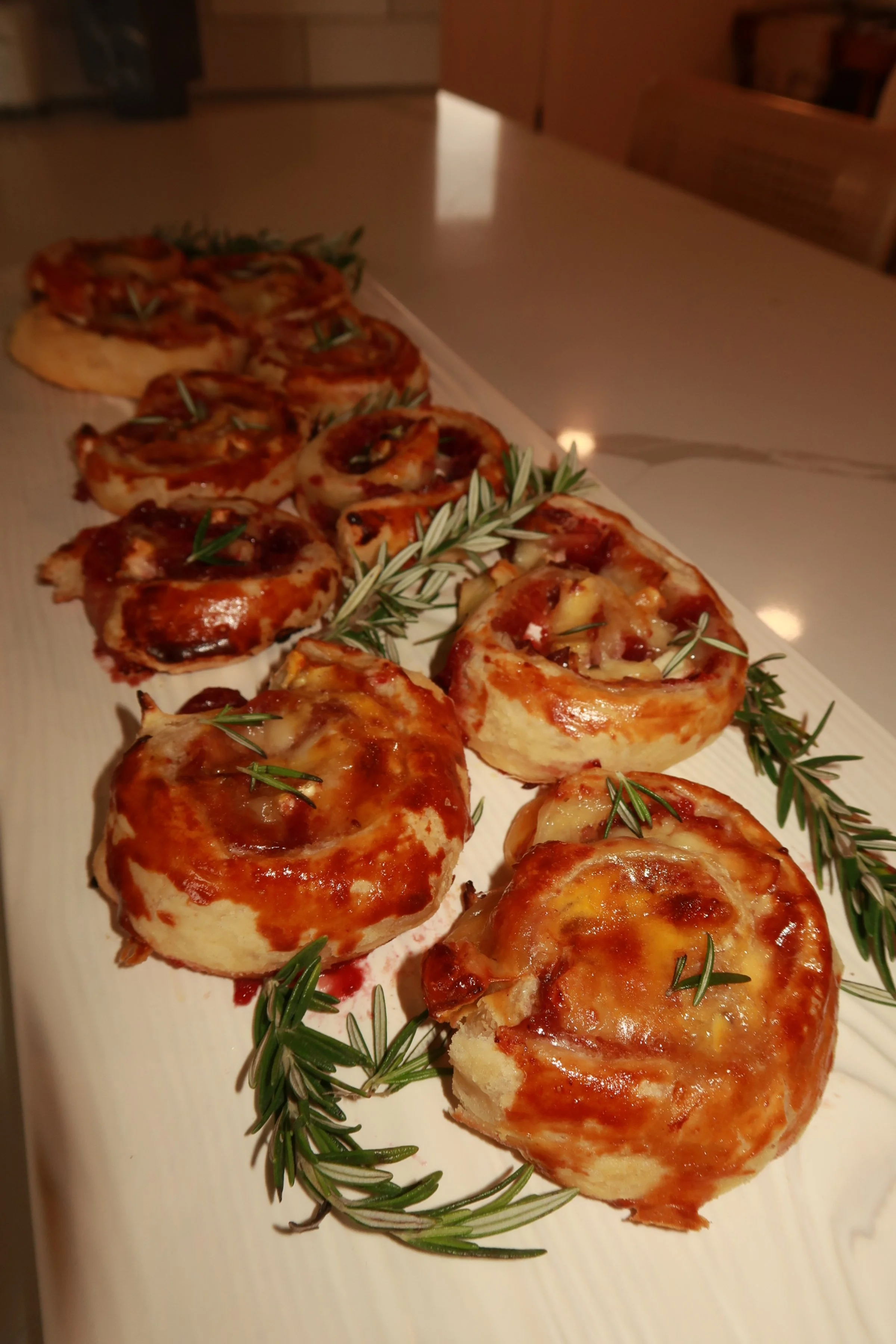 Baked mini pizzas on a white serving tray garnished with sprigs of rosemary.