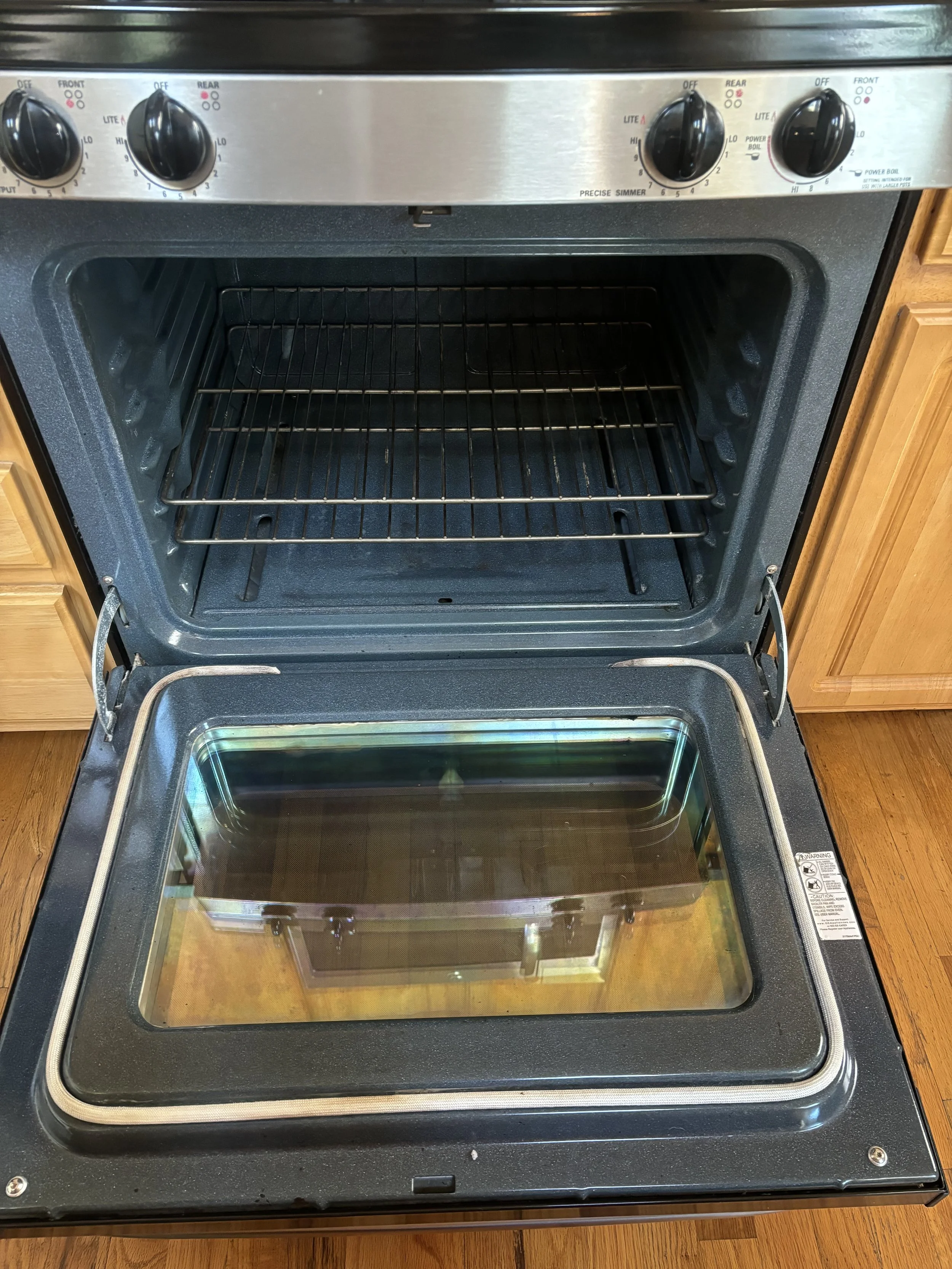 An open oven with a glass door, inner rack, and control knobs on the top panel.