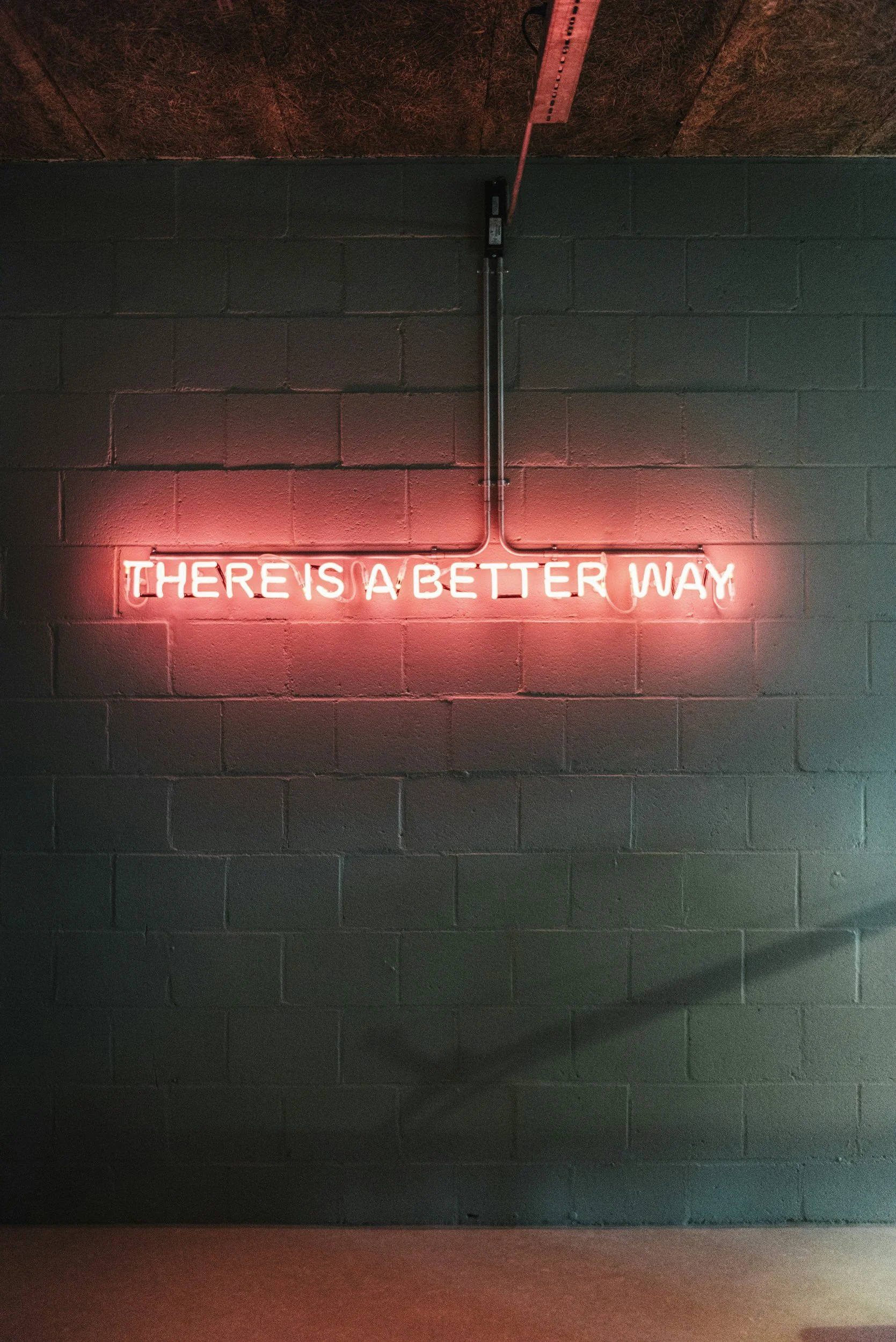 Neon sign on gray brick wall reads 'There is a better way' in pink text.
