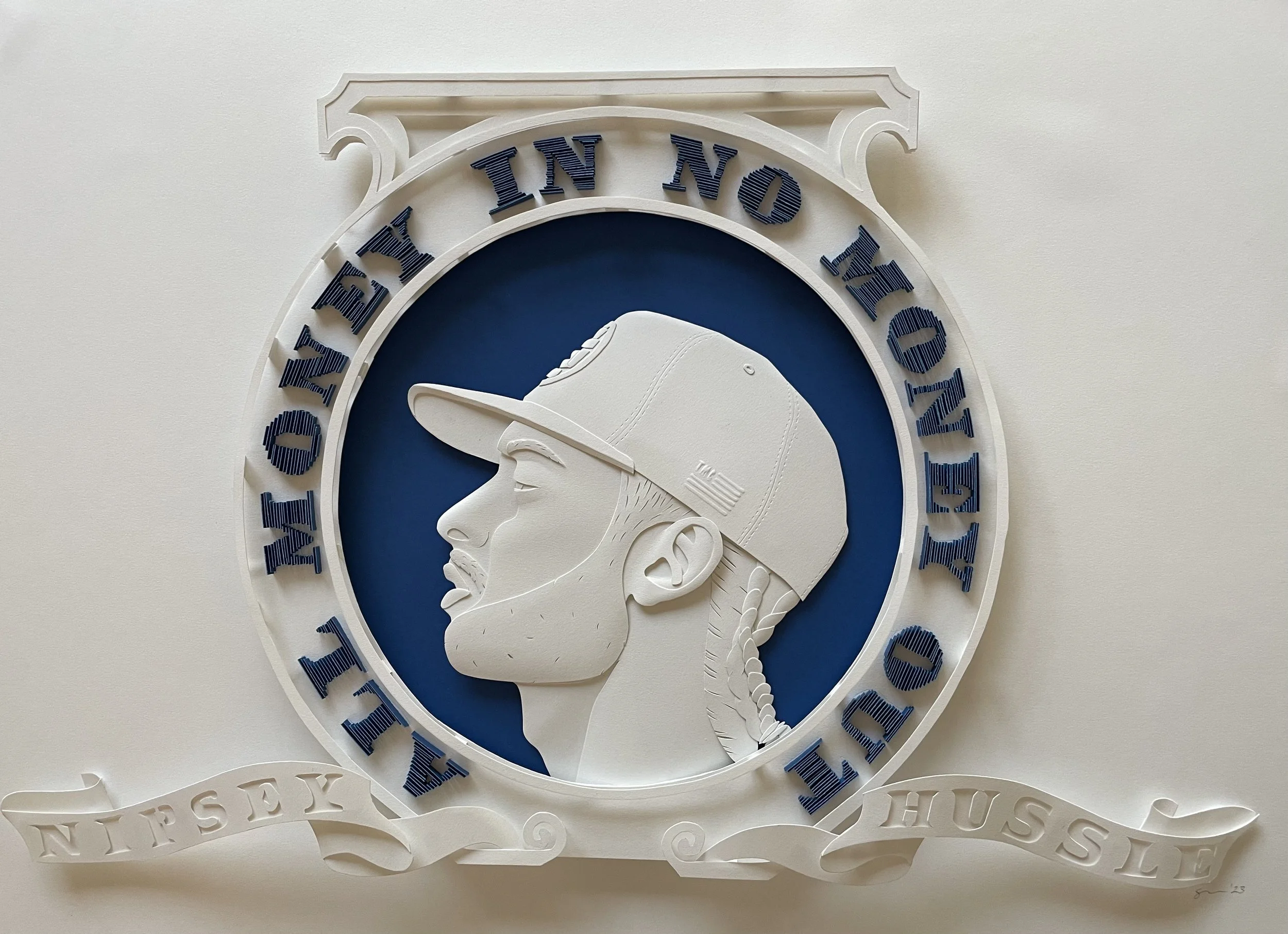 Paper sculpture of Nipsey Hussle. The picture is set in a crest encircled with his motto. 