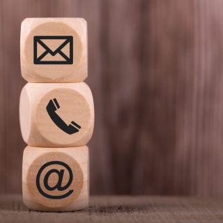 Three wooden blocks with icons for email, phone, and '@' symbol, stacked vertically on a wooden surface with a wooden background.