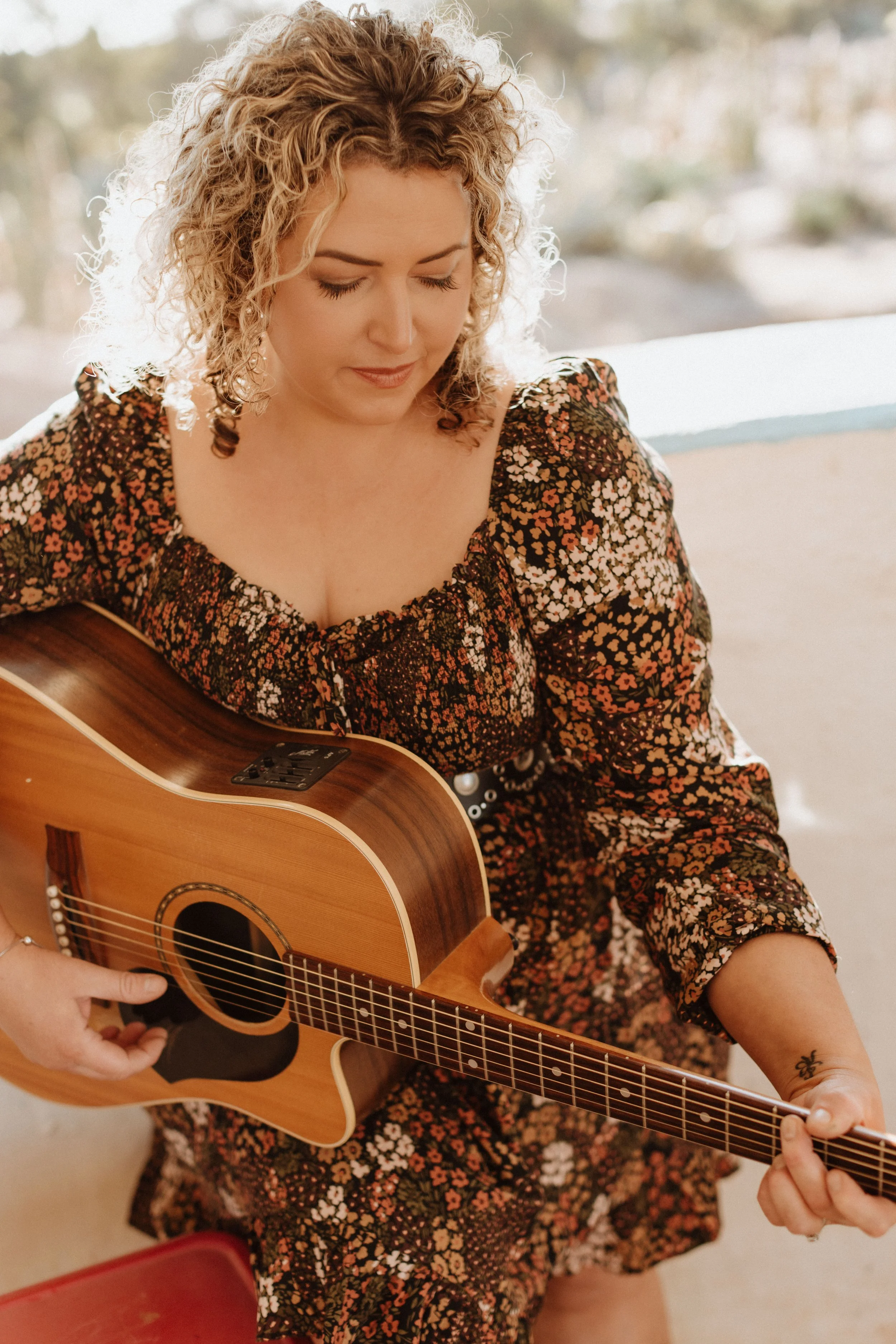 A woman with curly blonde hair playing an acoustic guitar indoors.