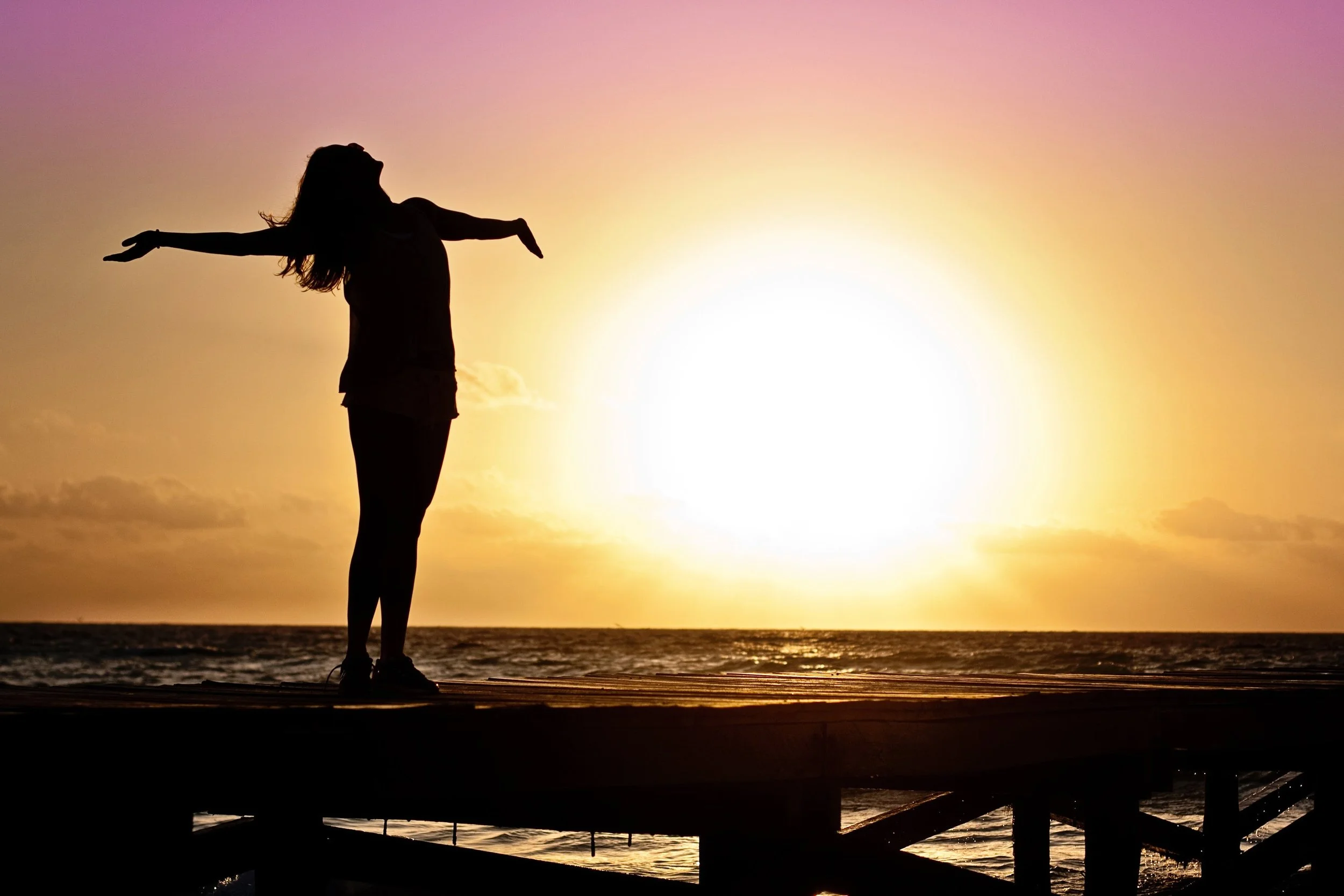 Woman standing with arms joyously outstretched in front of sunrise at the ocean