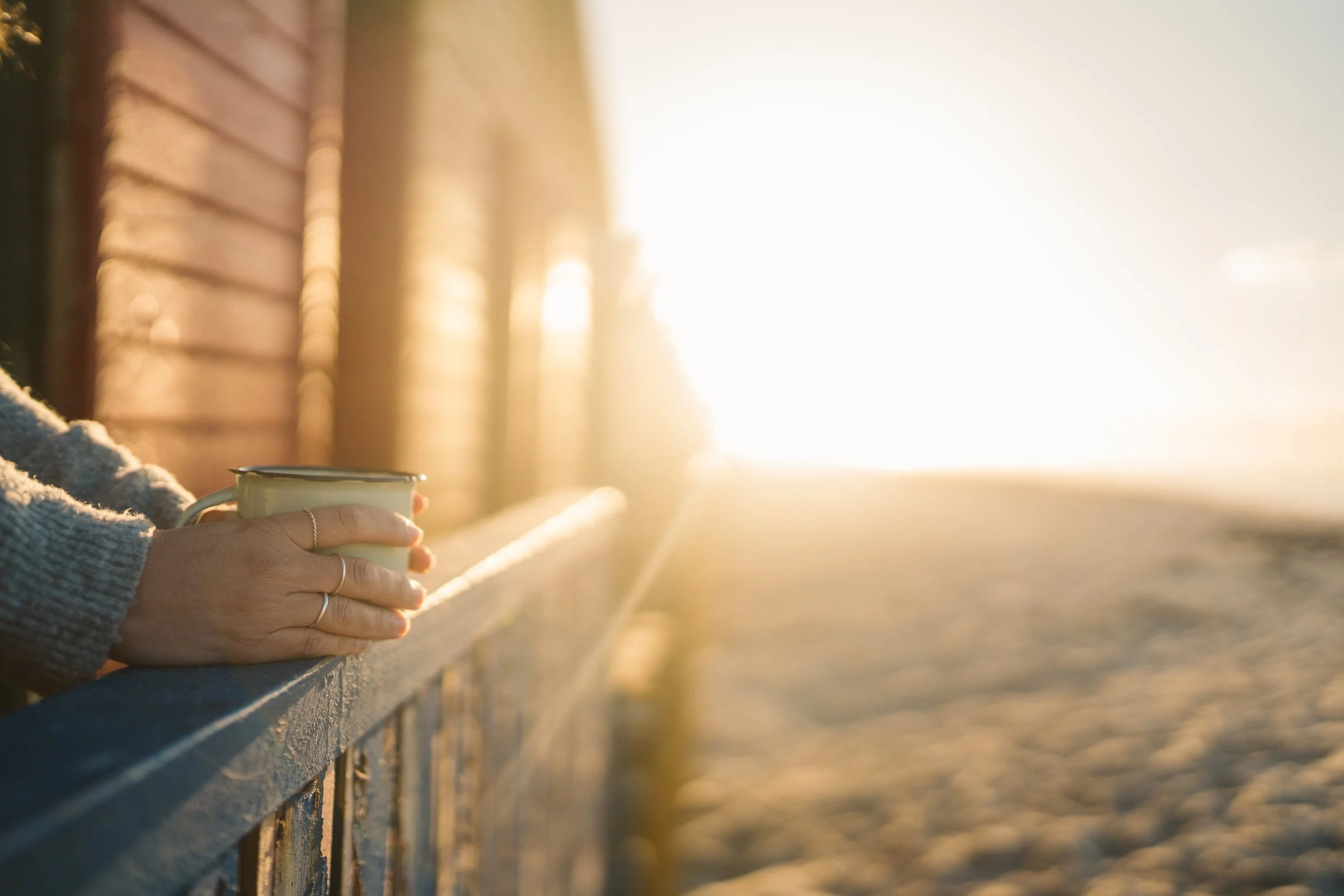 Close up of person holding coffee mug in front of a sunrise