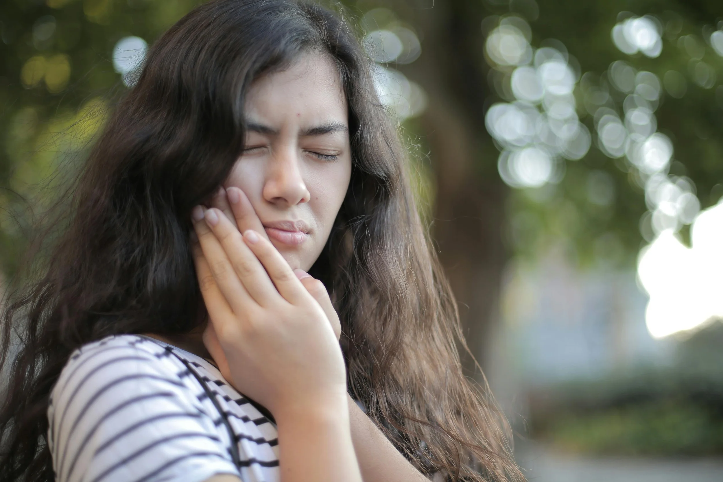 Woman holding her jaw with both hands due to jaw pain and TMJ discomfort