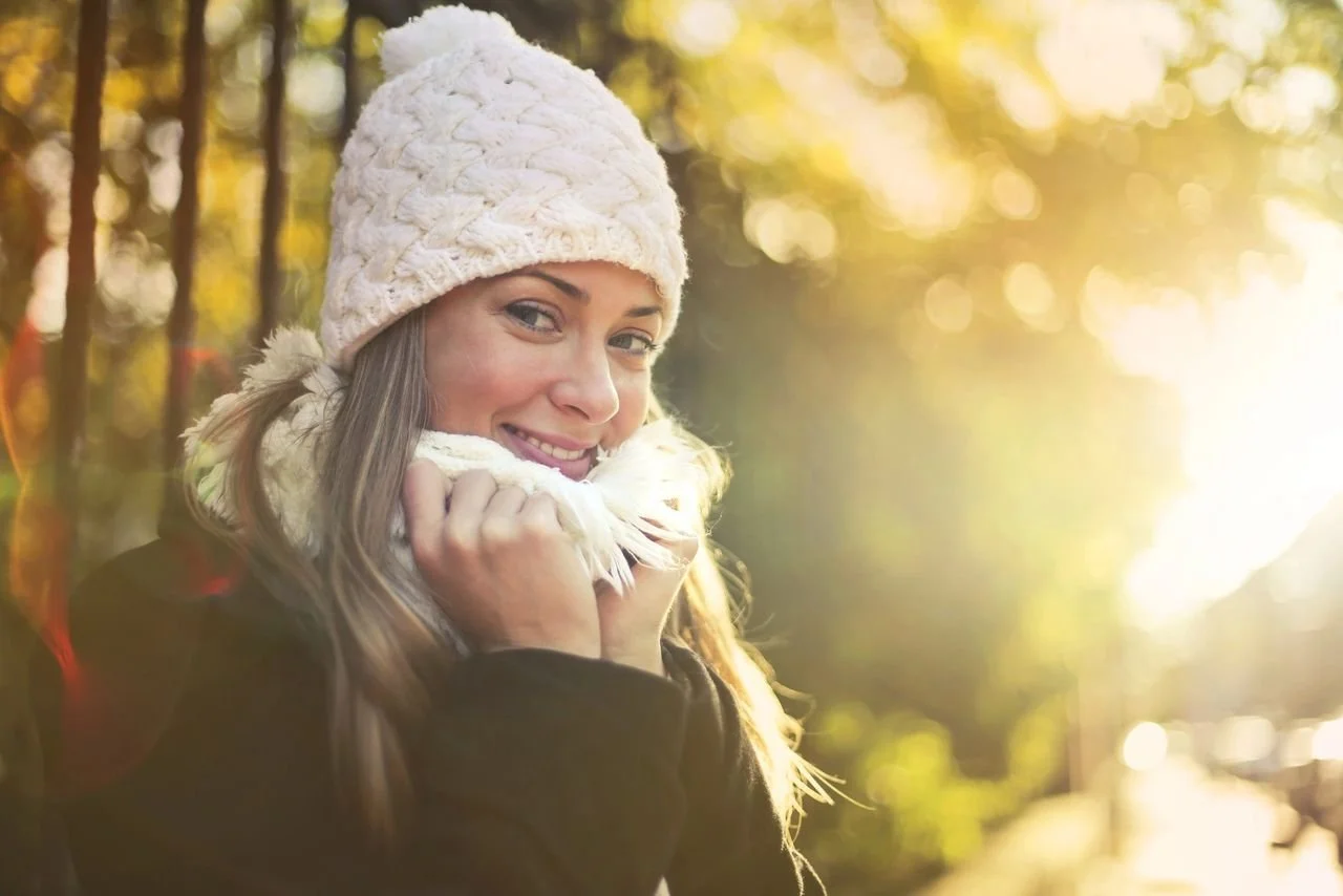 Woman smiling outdoors in the winters sun wearing a scarf and beanie