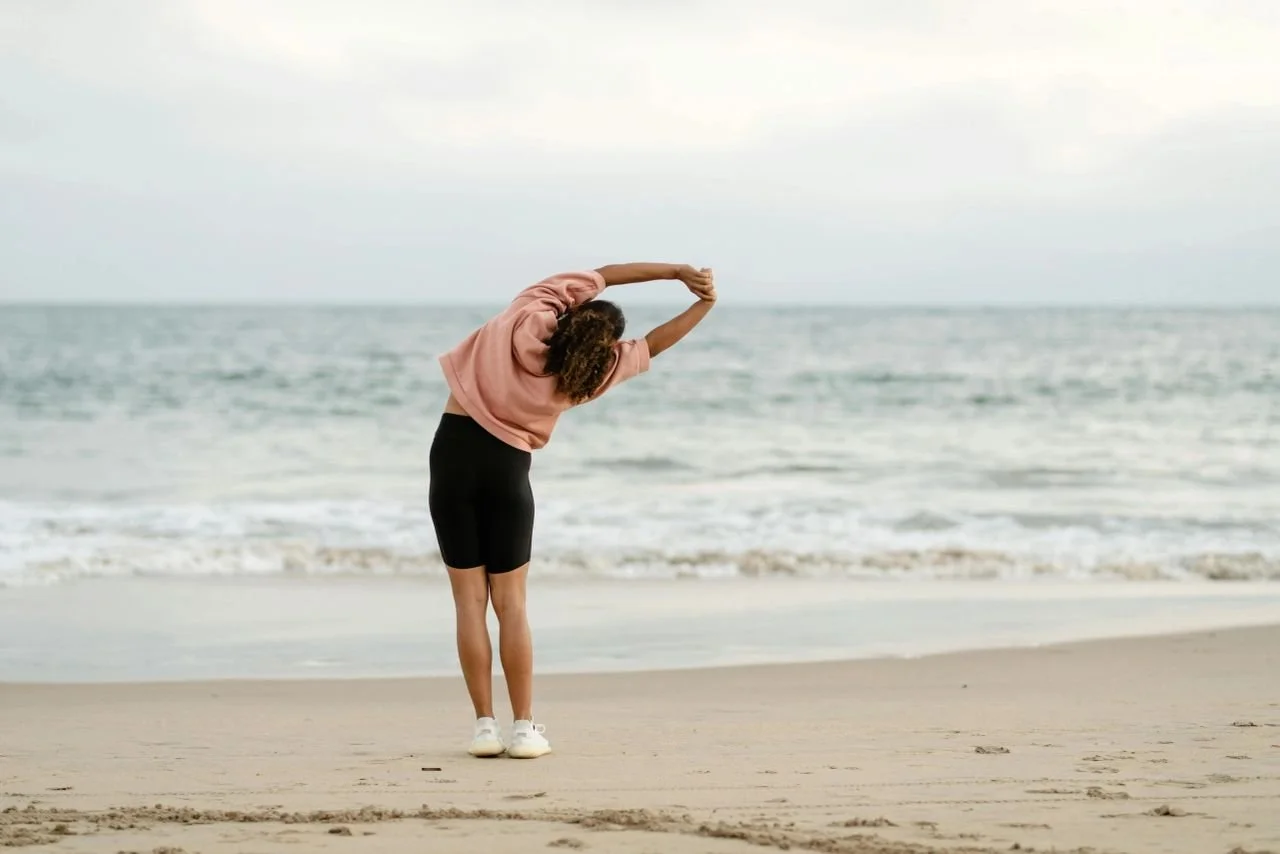 Lady doing side stretch at the beach looking over the ocean