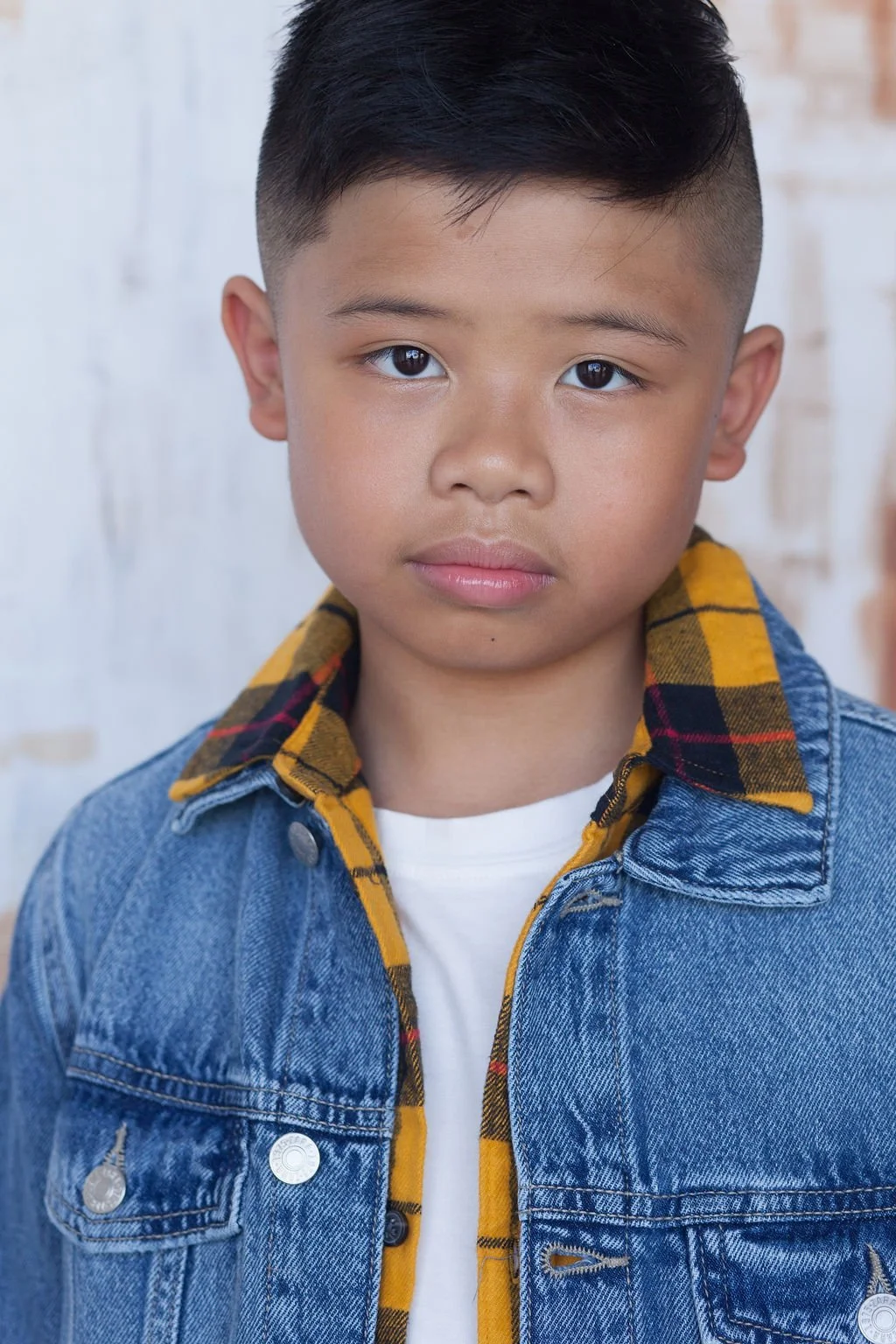 Sol Andres in a blue denim jacket with yellow checkered flannel shirt standing behind an industrial white brick wall