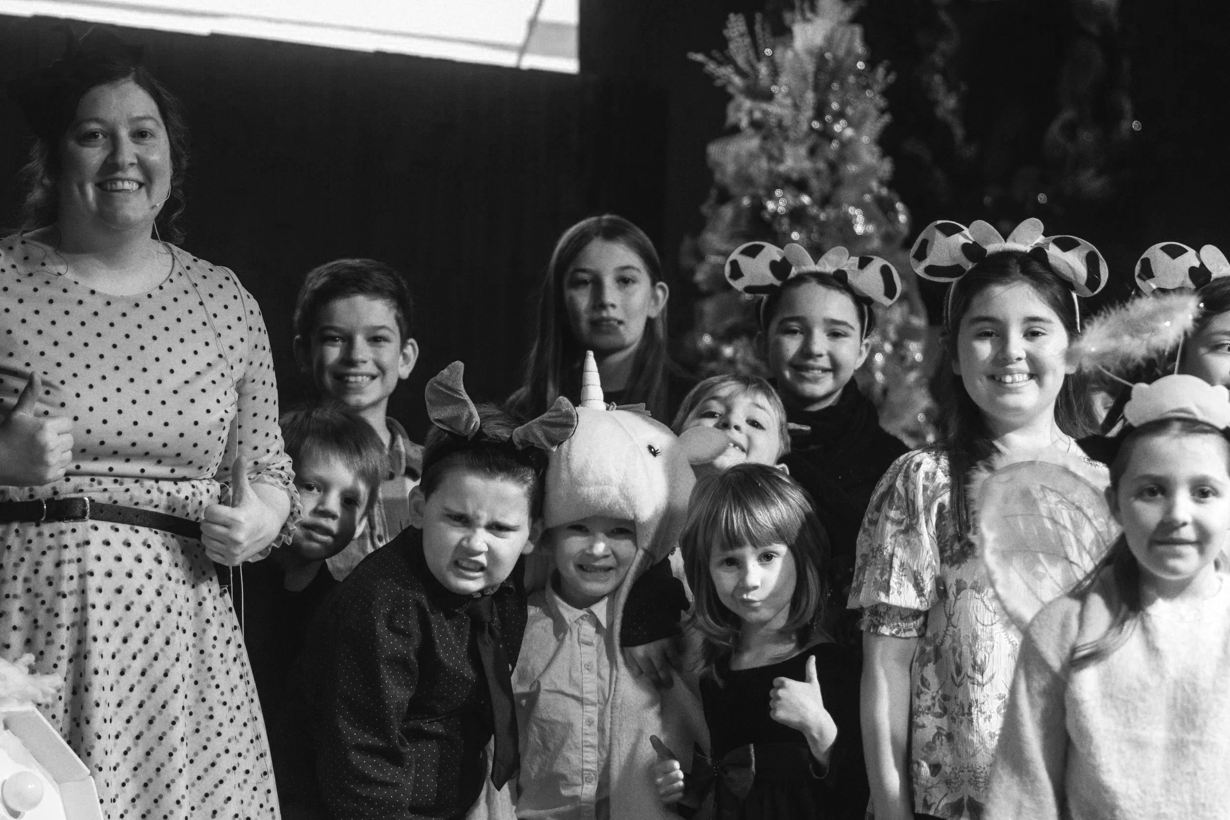 Group of children and a woman dressed in costumes at a holiday party in front of a Christmas tree