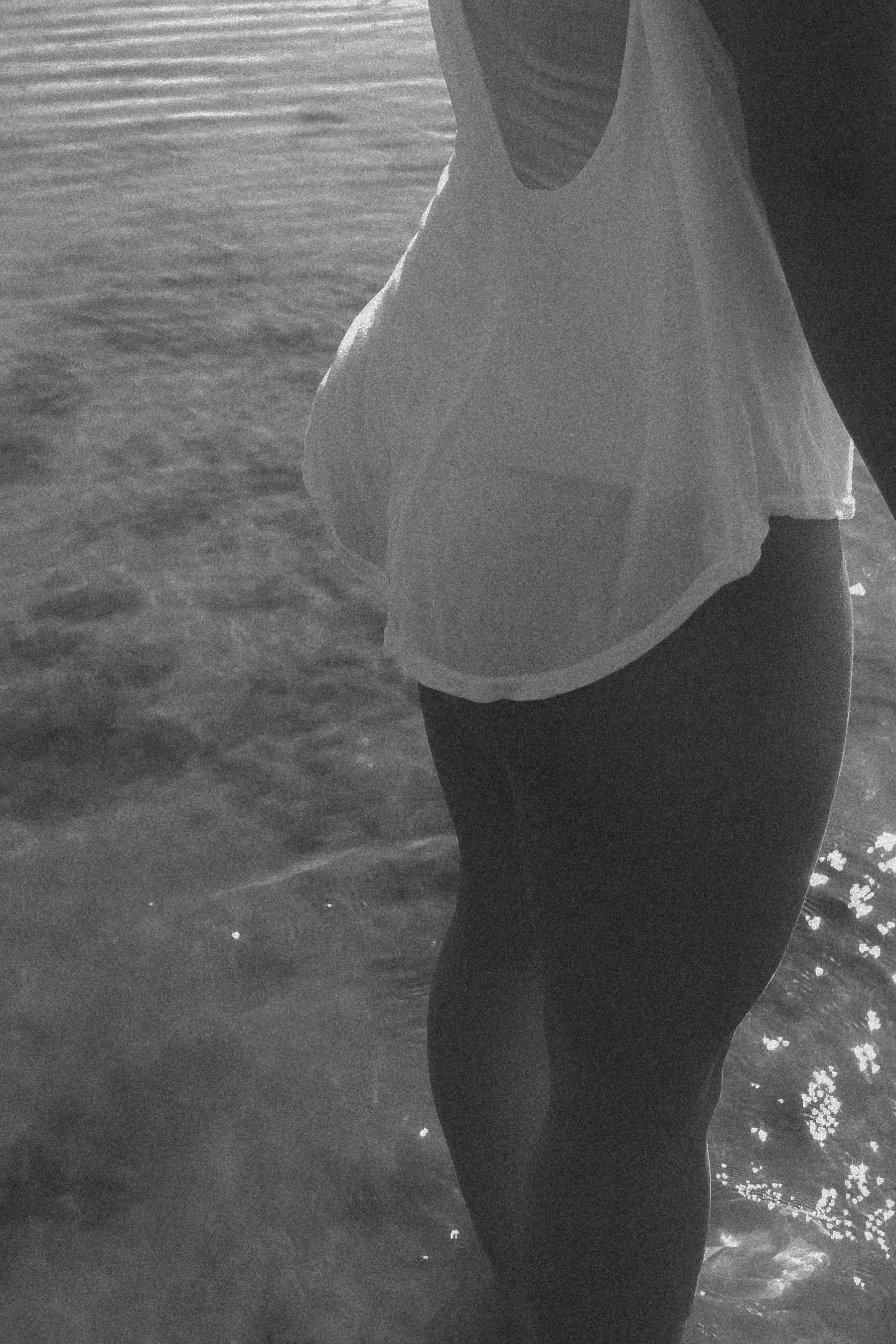 A person standing in water, wearing a sleeveless white top and dark pants, with water reaching just above the knee.