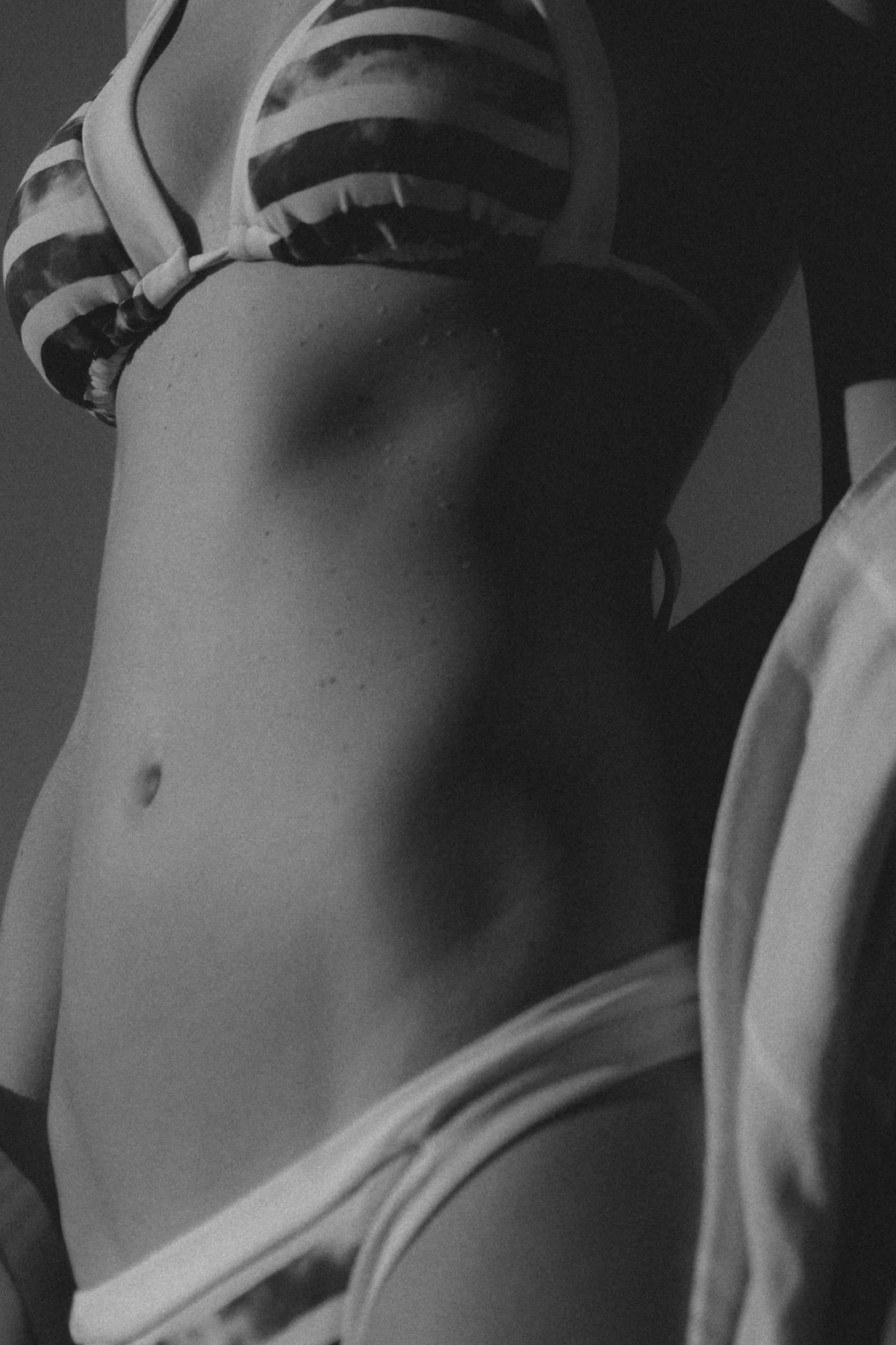 Close-up of a woman's torso, wearing striped bikini top and shorts, in black and white.