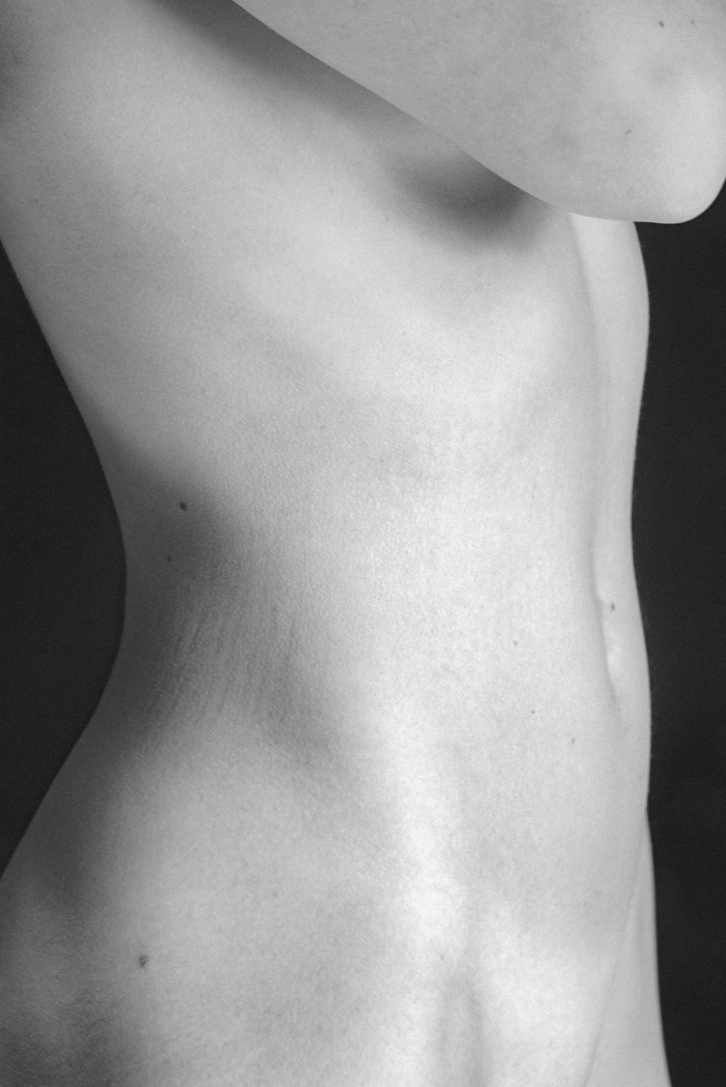 A close-up black and white photo of a person's bare torso, focusing on the side profile from the shoulder to the waist.