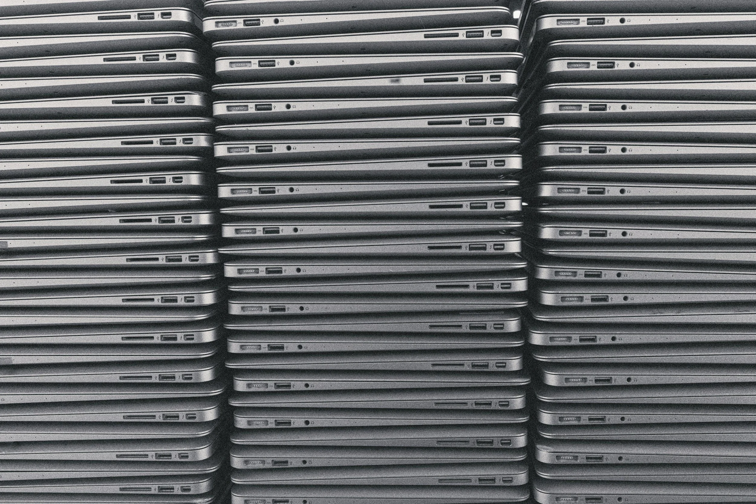 A large stack of laptops arranged in multiple rows with the side view displaying ports and profiles.