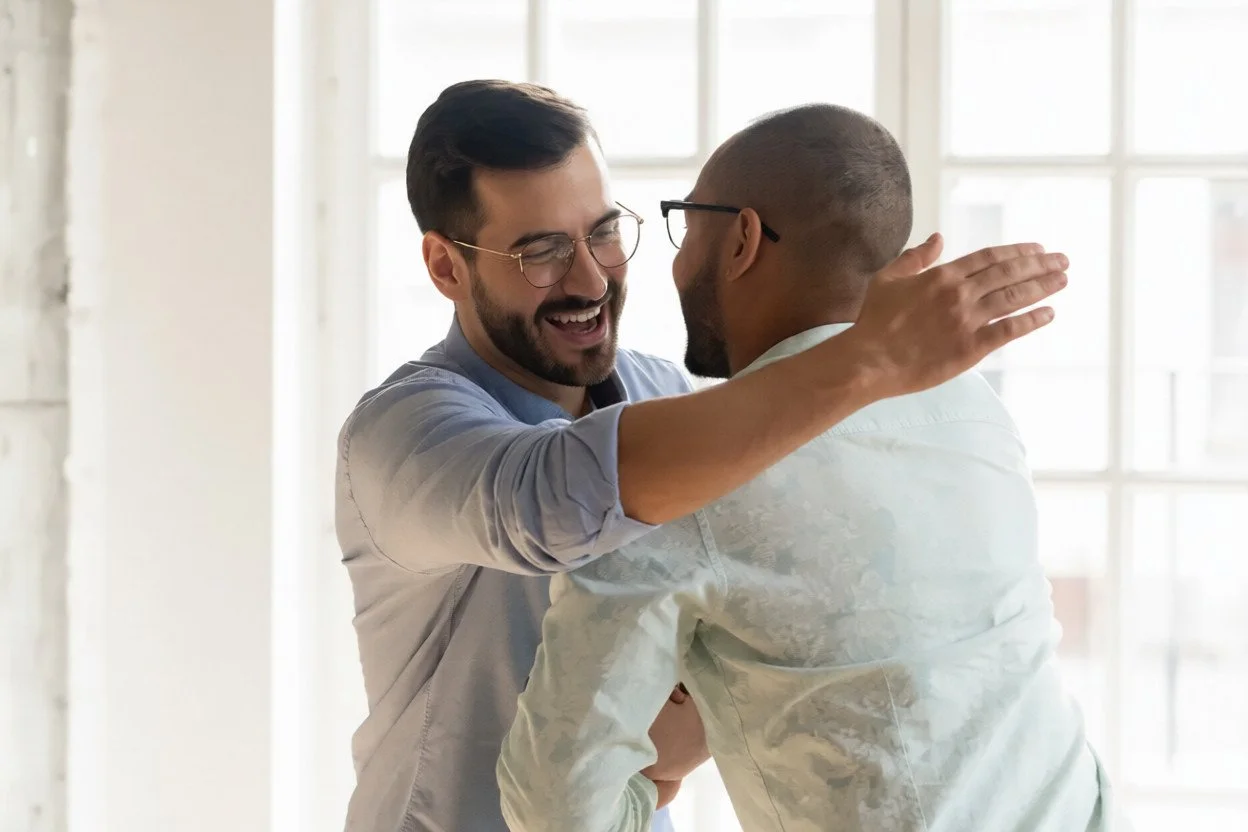 amigos-masculinos-sonrientes-abrazan-el-hombro-de-grifo-reuniéndose-en-interiores-los-hombres-caucásicos-gafas-se-sienten-muy-168453788 (1).jpg