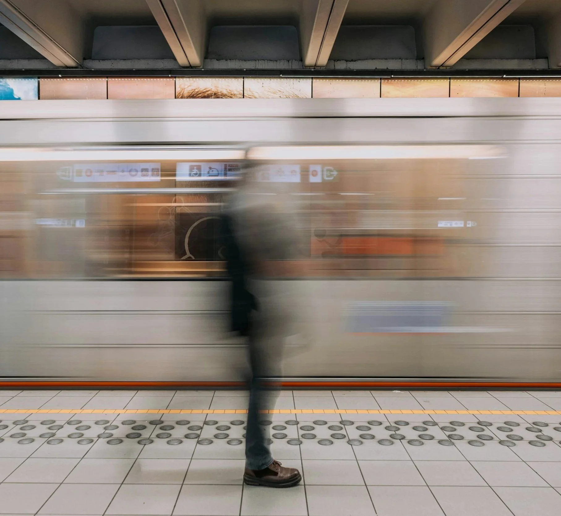 Moving train at a subway station with a blurred figure of a person standing on the platform