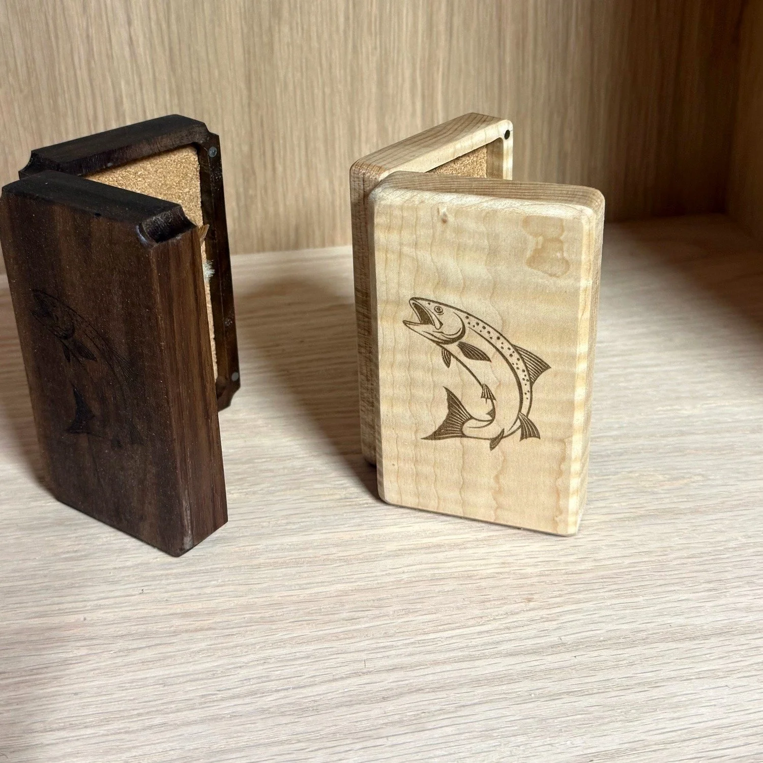 Curly maple and walnut fly boxes side by side, the maple showing its engraved leaping trout lid